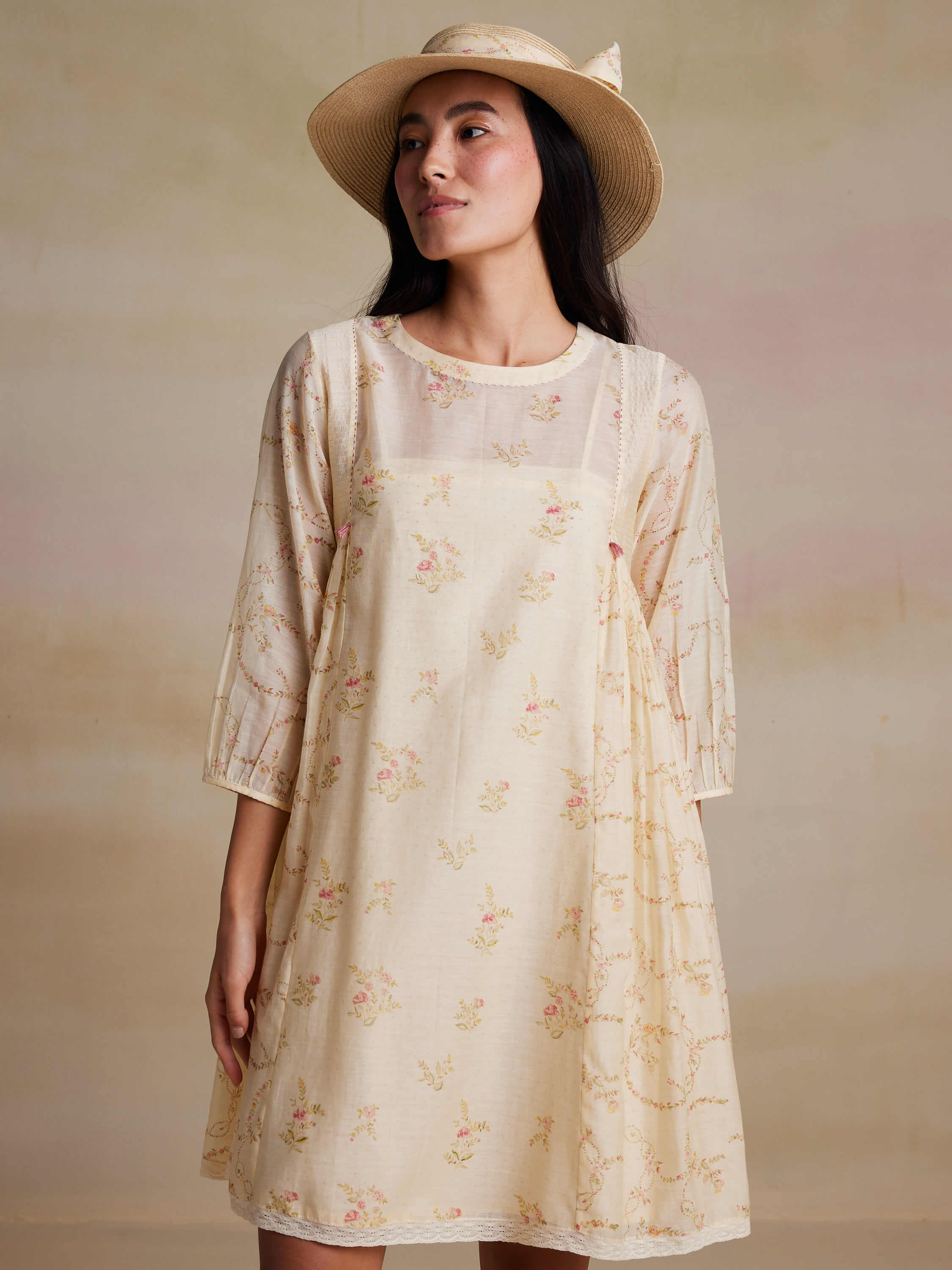 Woman wearing a floral dress and sunhat in neutral background.