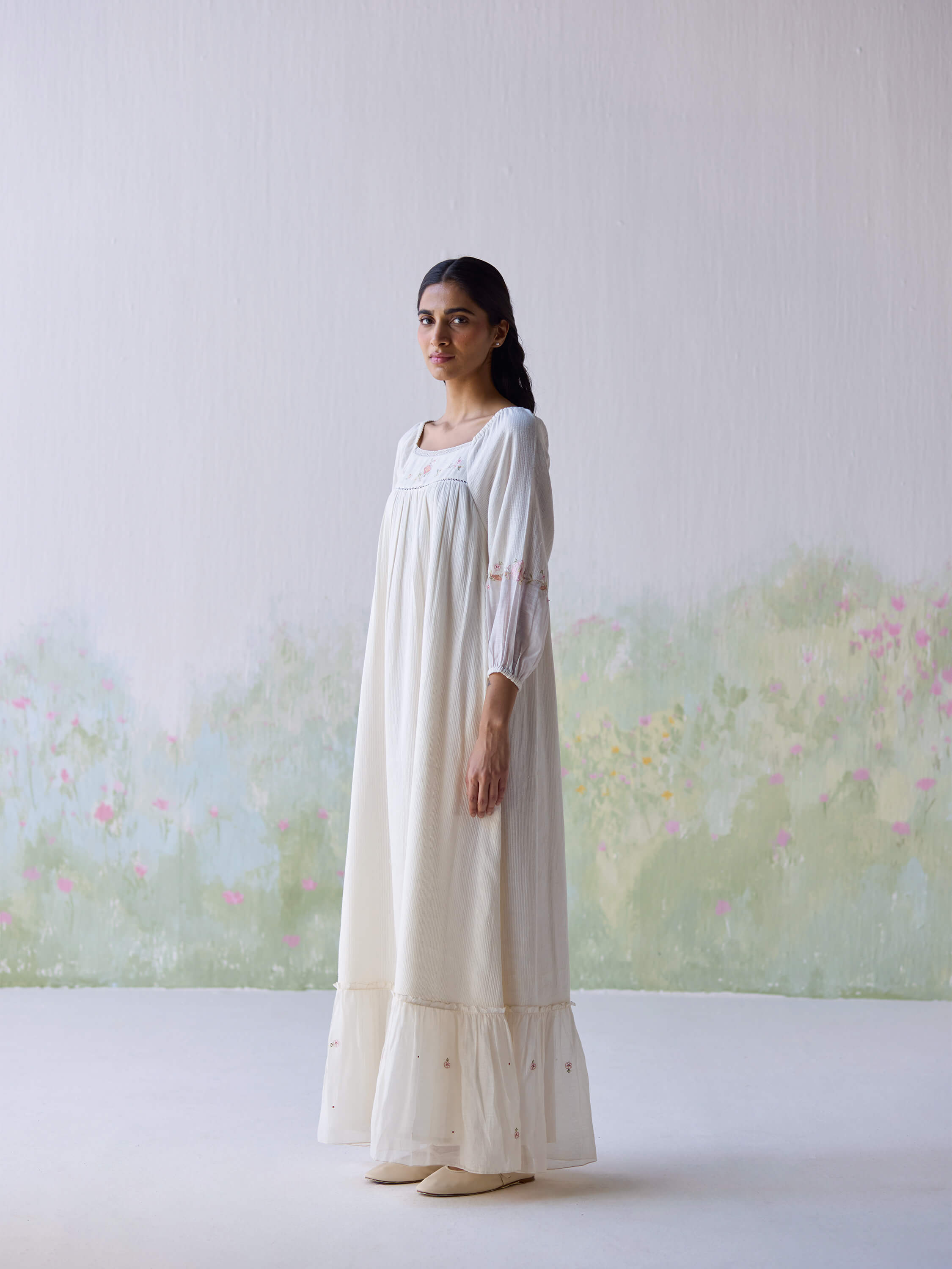 Elegant model in Belle Maxi Dress against floral backdrop.