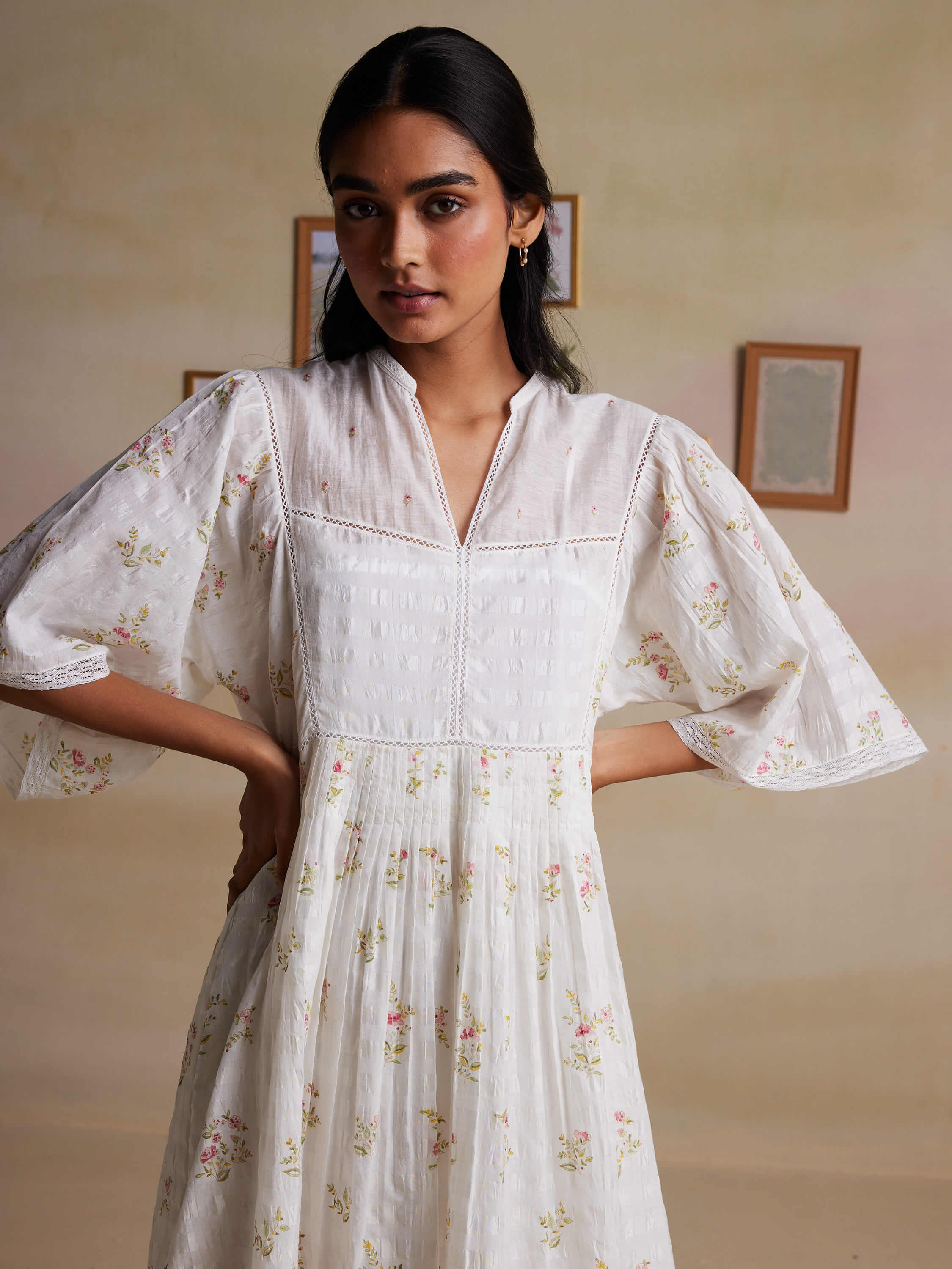 Woman wearing floral white dress with loose sleeves, posing indoors.