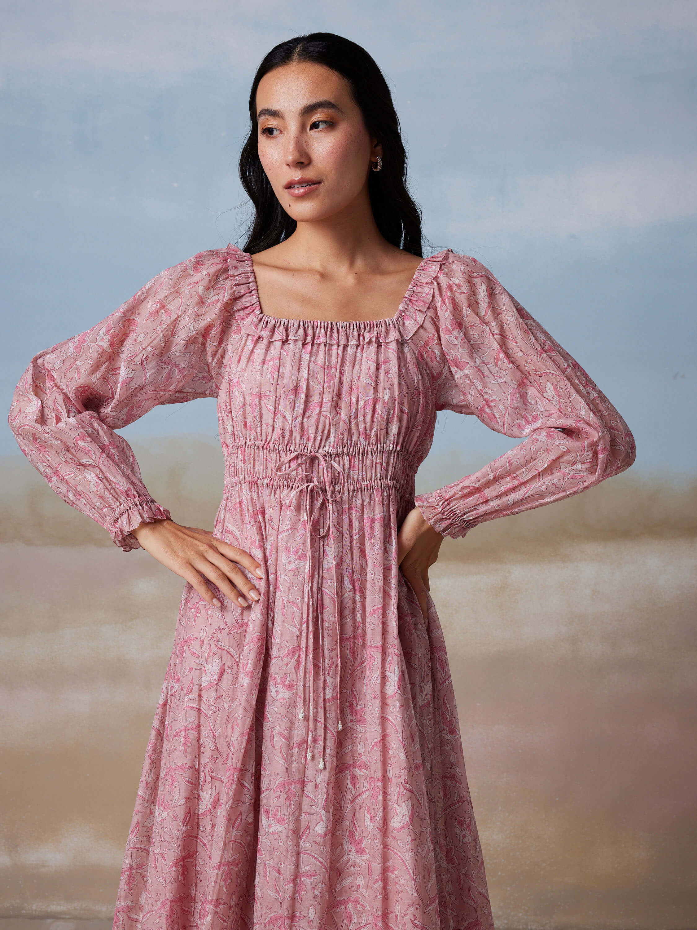Woman in pink long-sleeve dress with floral pattern, standing against blue background.