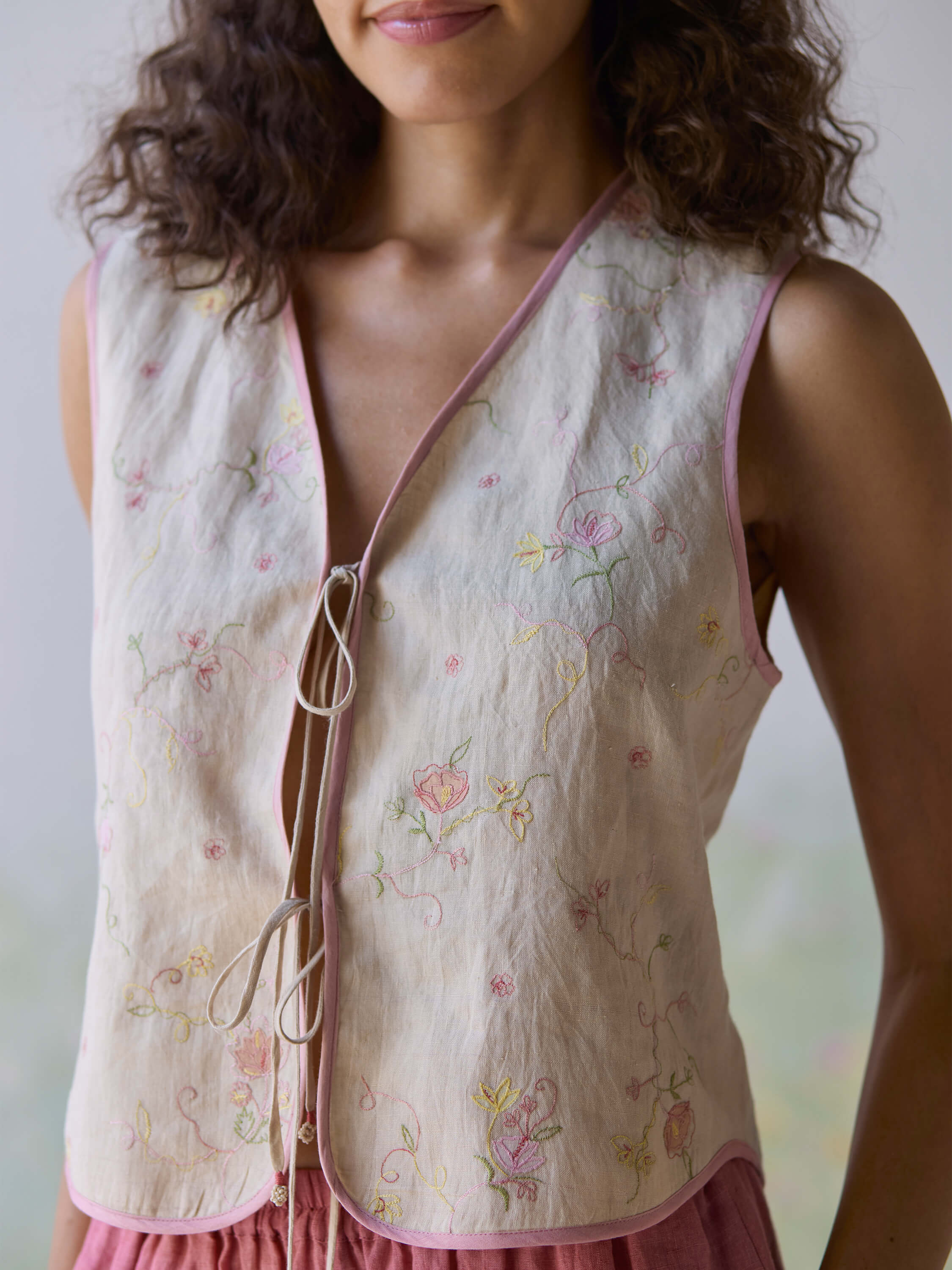 "Fanfare Linen Gilet featuring floral embroidery and delicate tie closure."