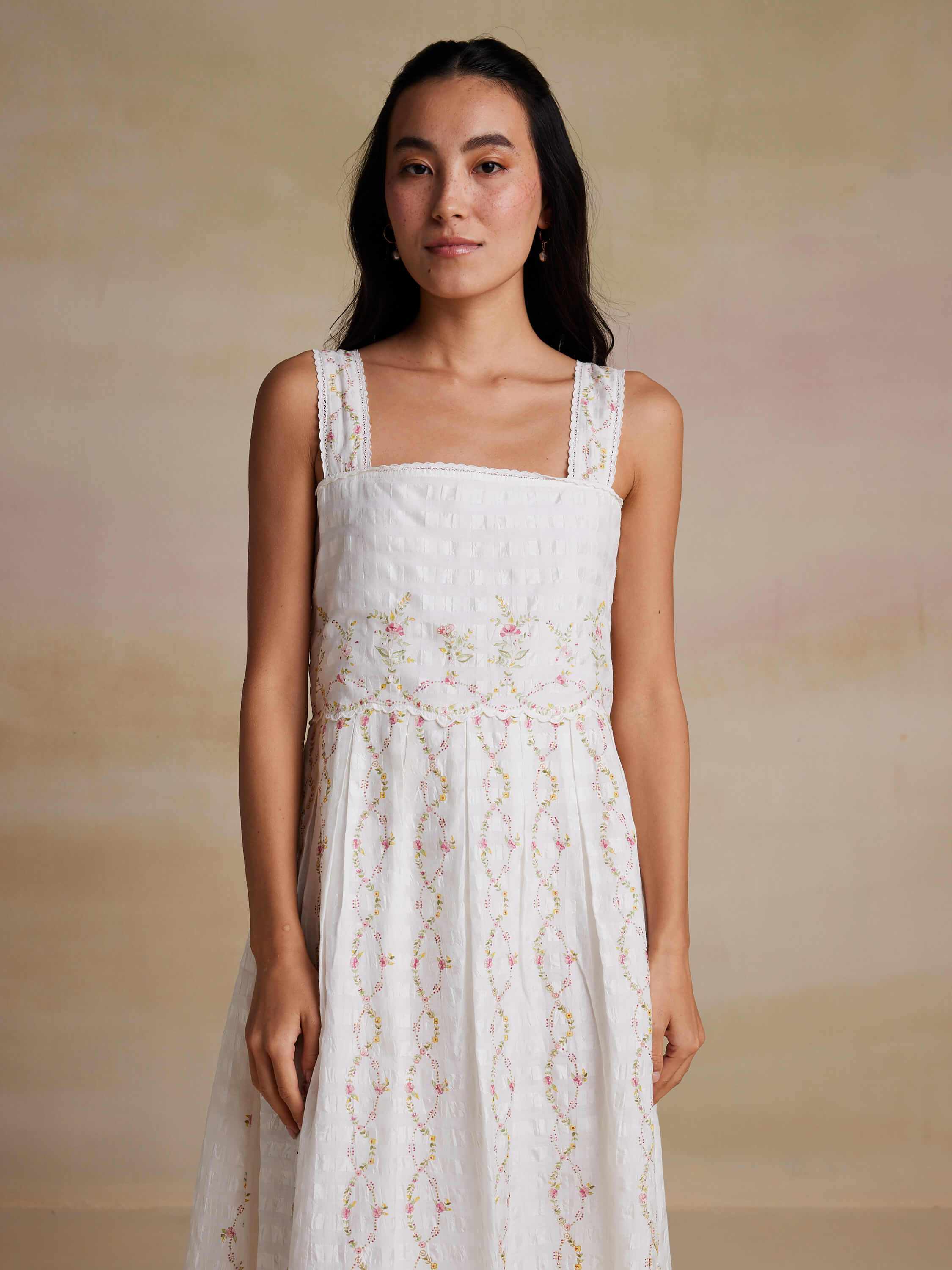Woman wearing white sleeveless dress with floral embroidery pattern.