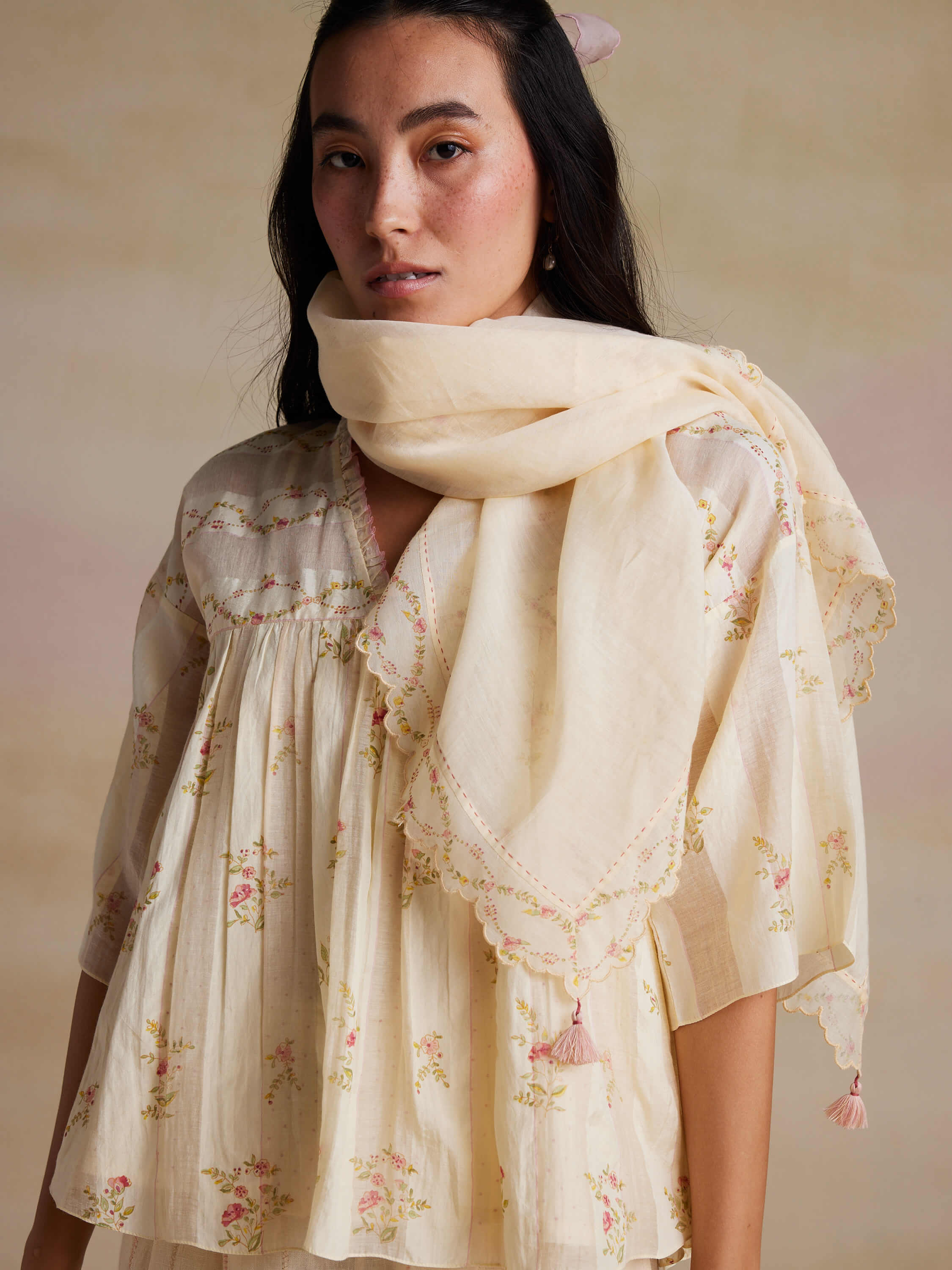 Woman in floral embroidered top and scarf, beige background.
