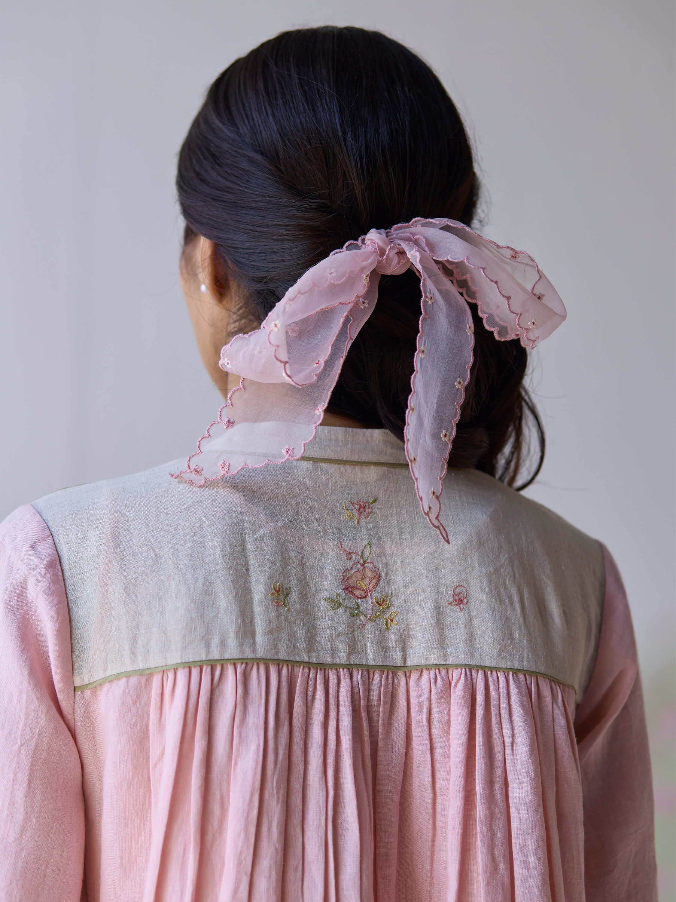 Back view of woman in pink linen dress with embroidered details.