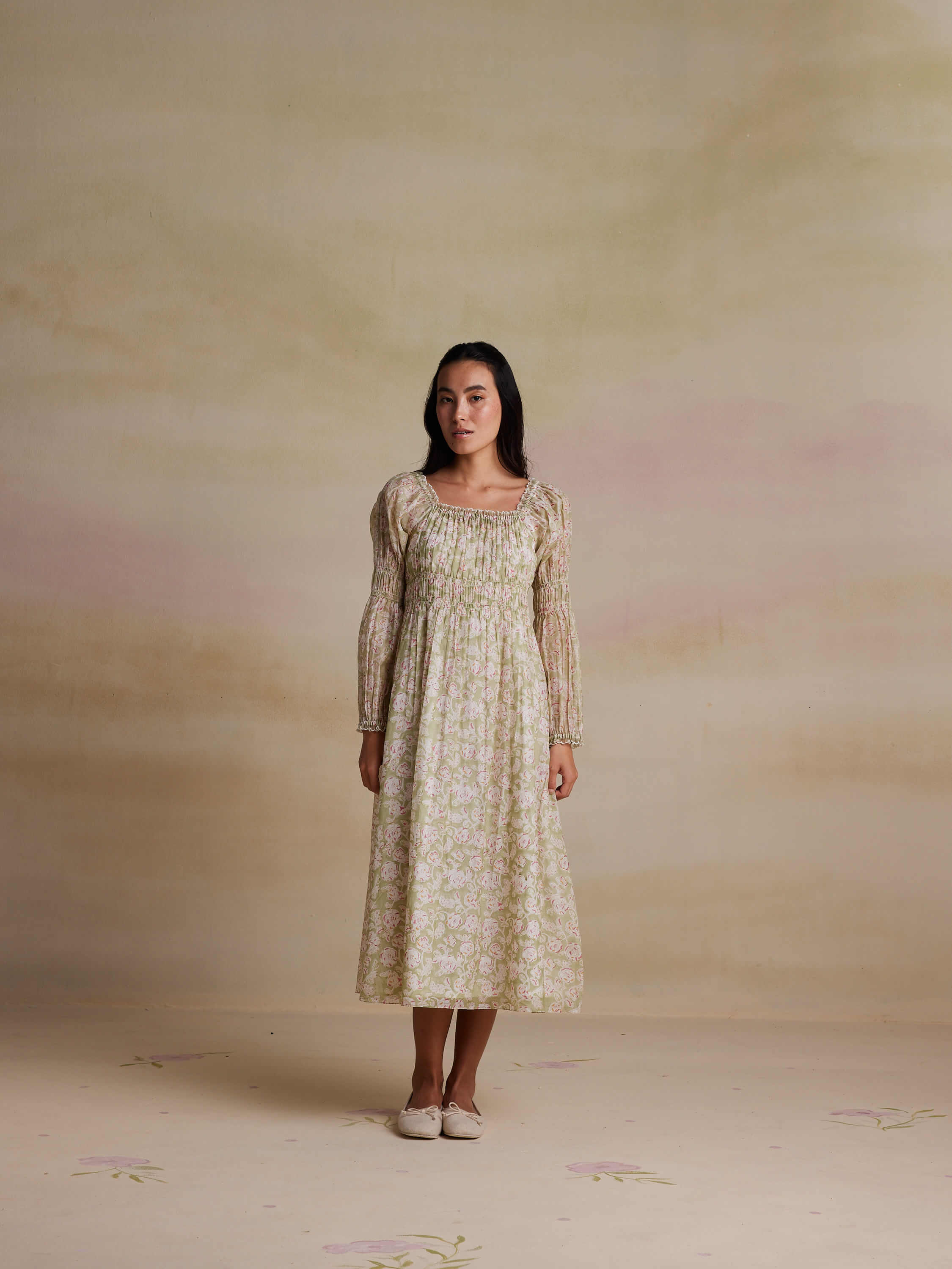 Woman in a long floral dress posing against a neutral background.