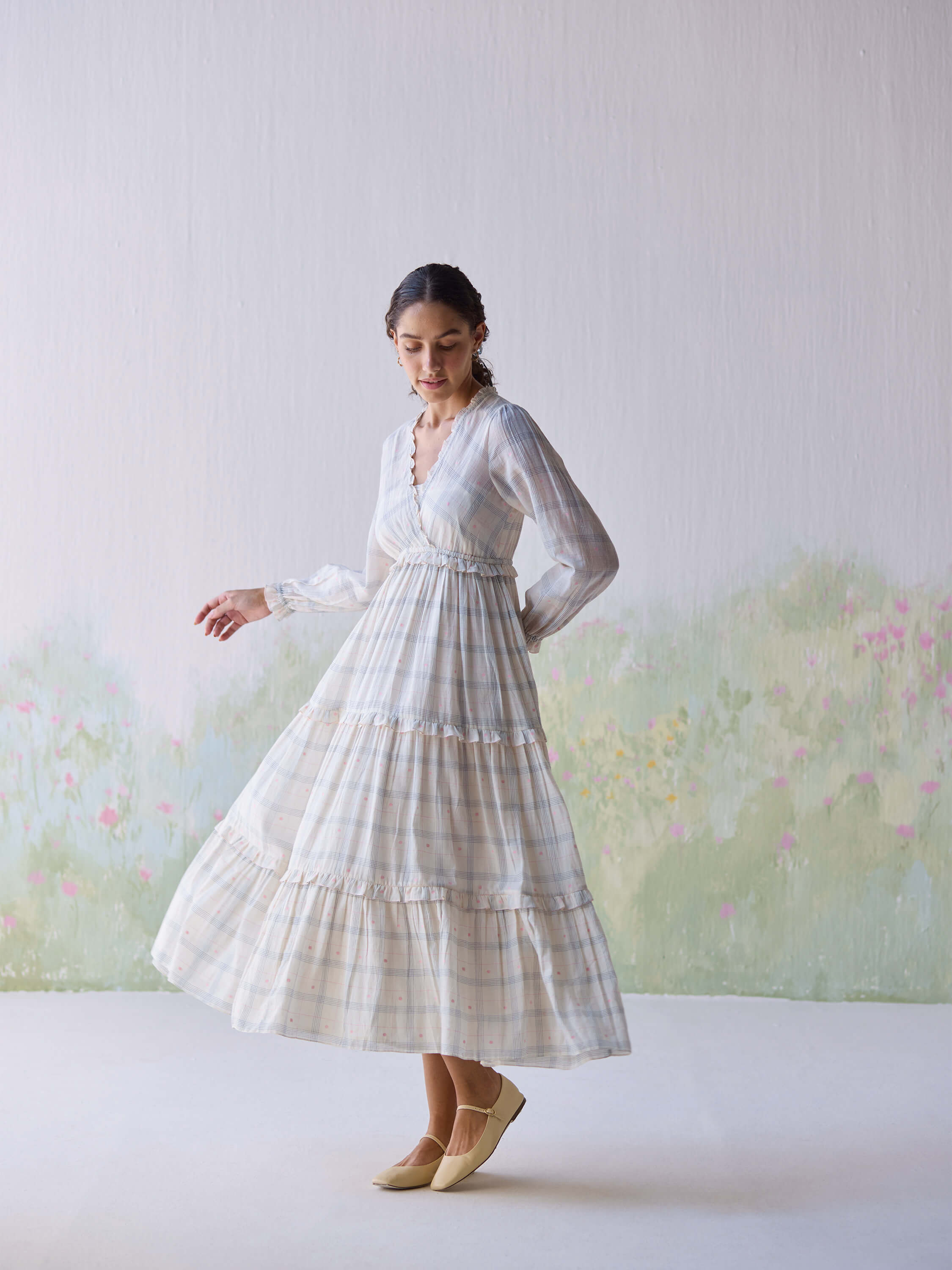 Elegant woman twirling in Paperdots Wrap Dress against floral backdrop.