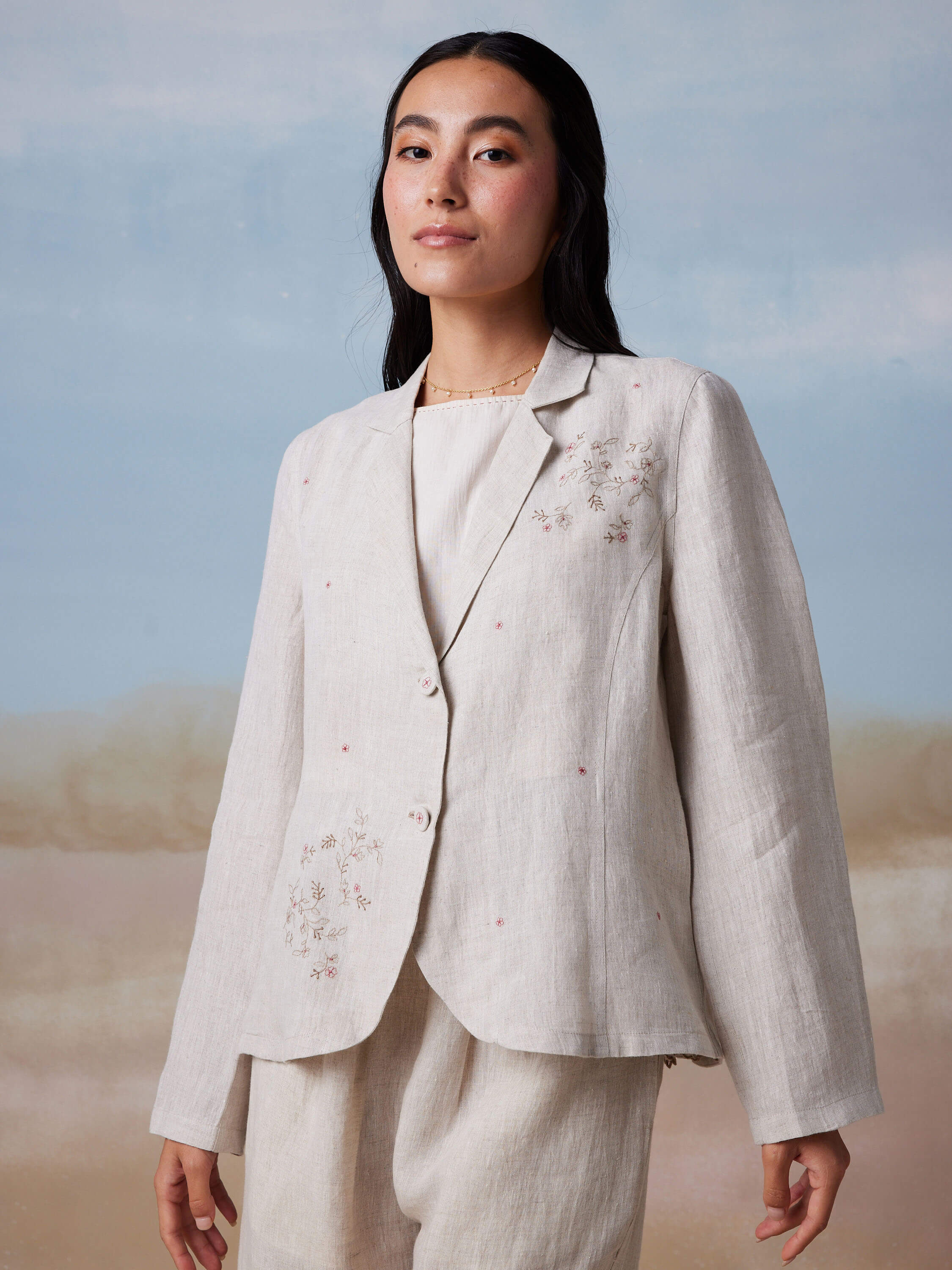 Woman wearing a light embroidered suit standing against a soft background.
