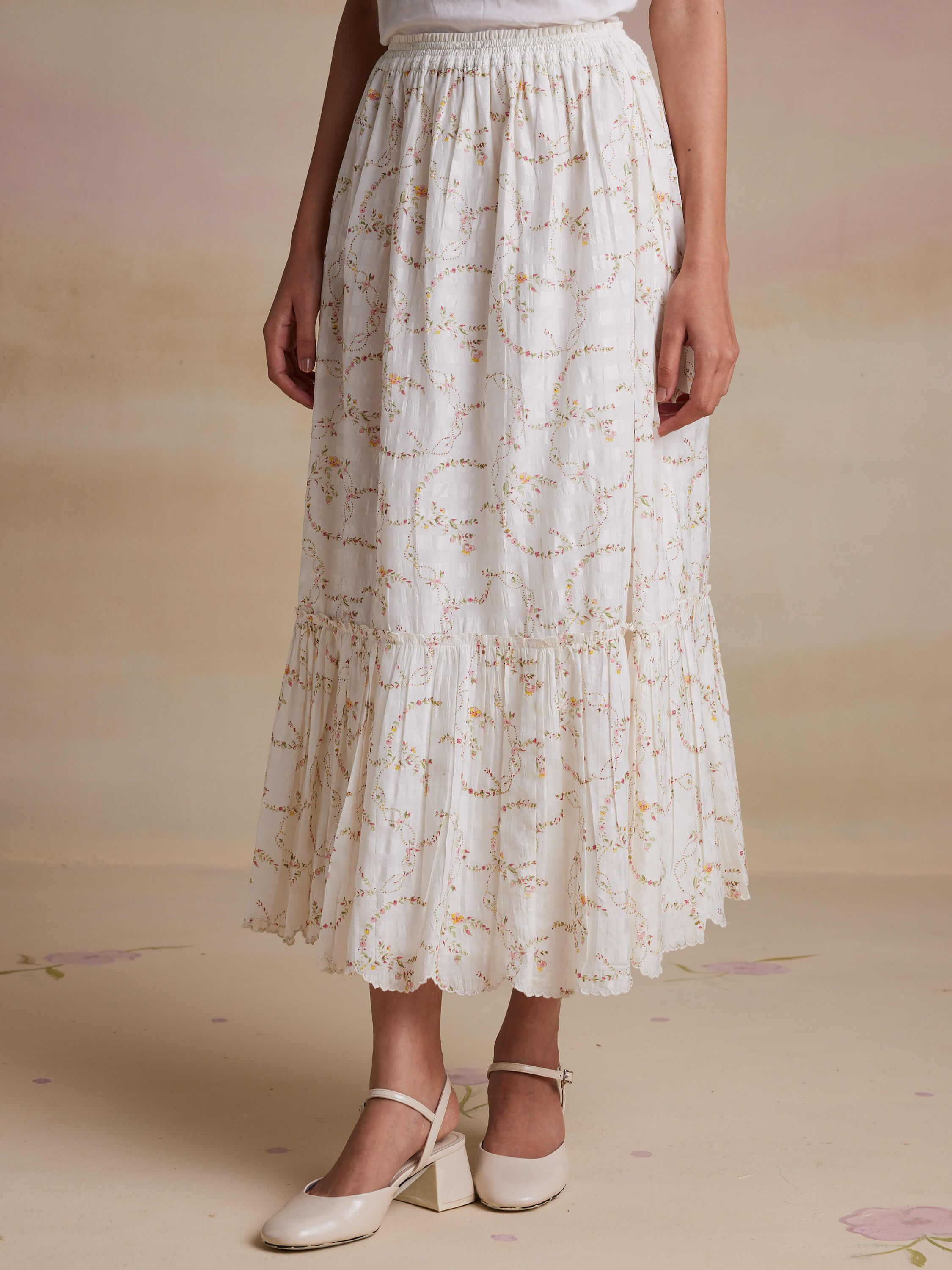 Woman wearing a white floral embroidered midi skirt with white block heels.