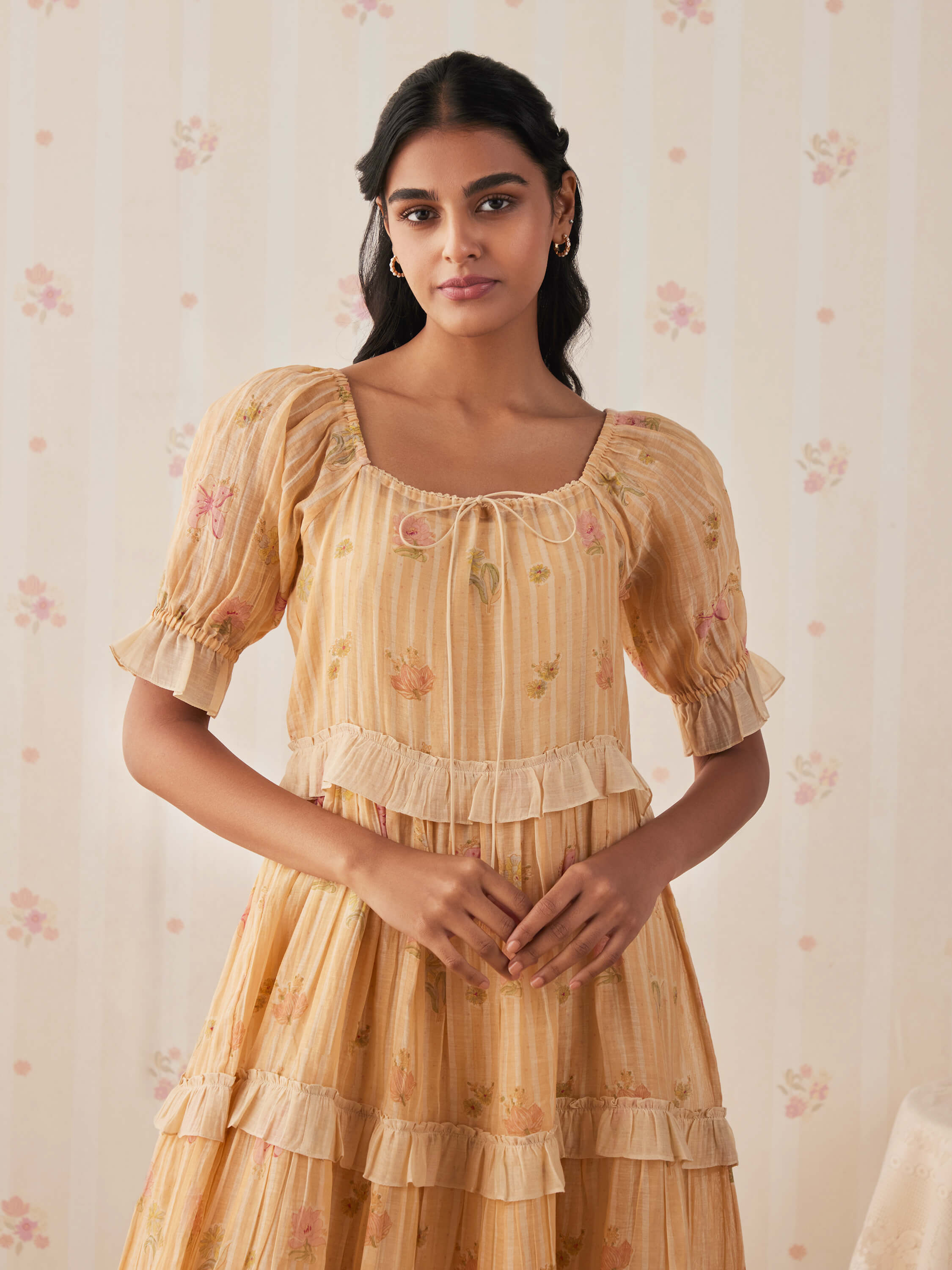 Woman wearing a floral yellow vintage dress against a floral wallpaper backdrop.