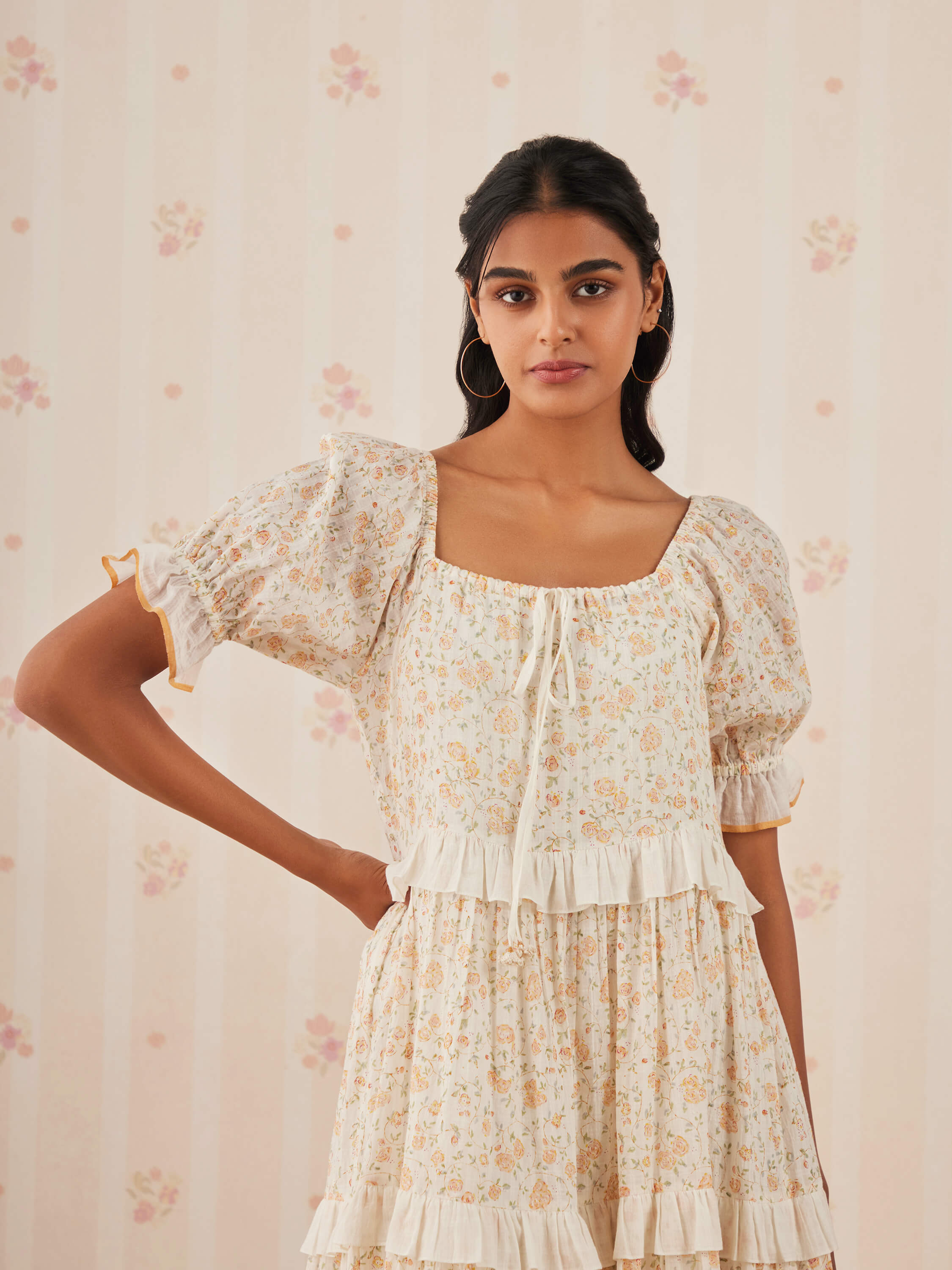 Woman in floral dress posing against a pastel floral background.