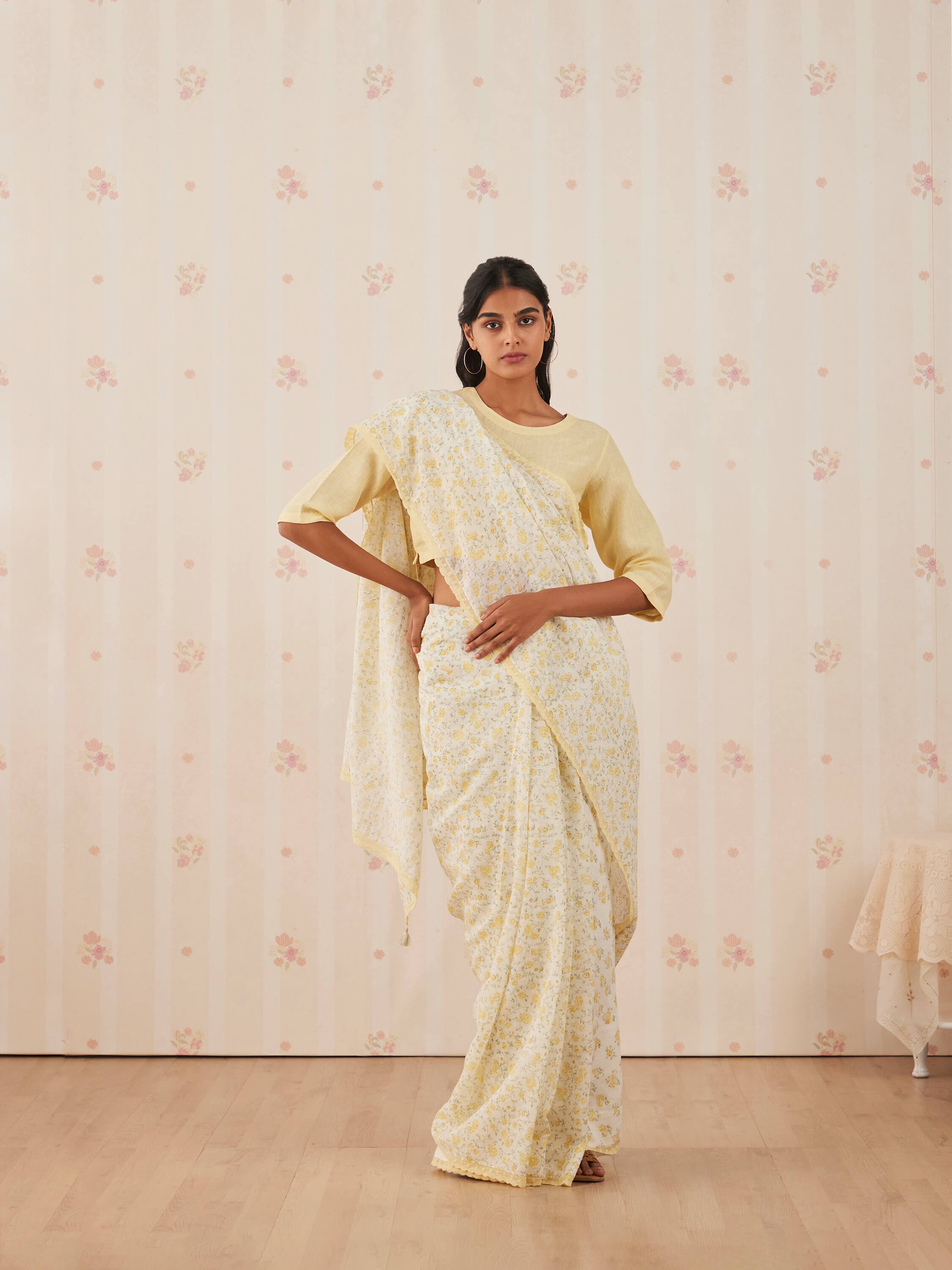 Woman wearing floral yellow saree in elegant indoor setting.