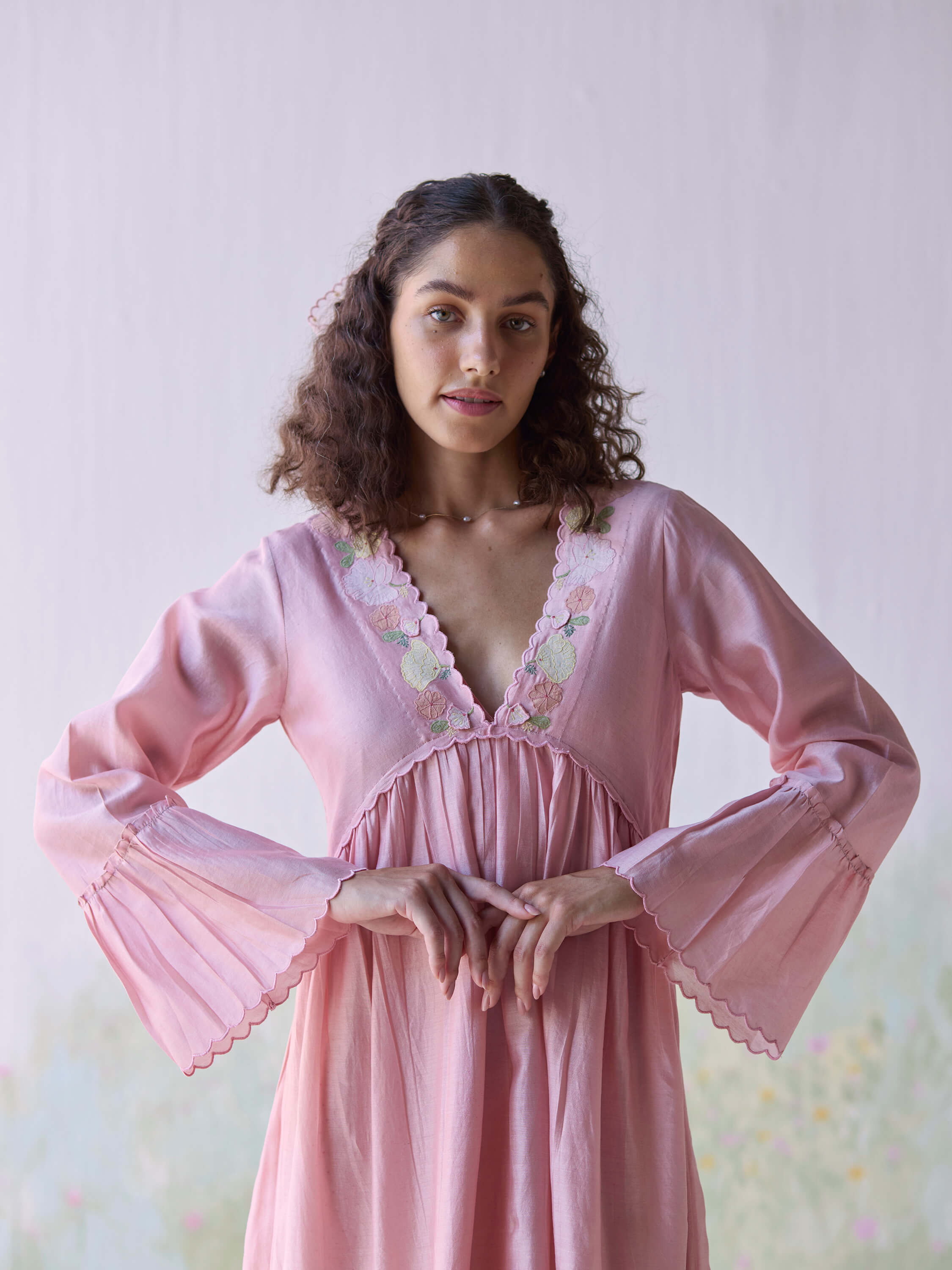 Woman in elegant pink dress with floral embroidery and flared sleeves.
