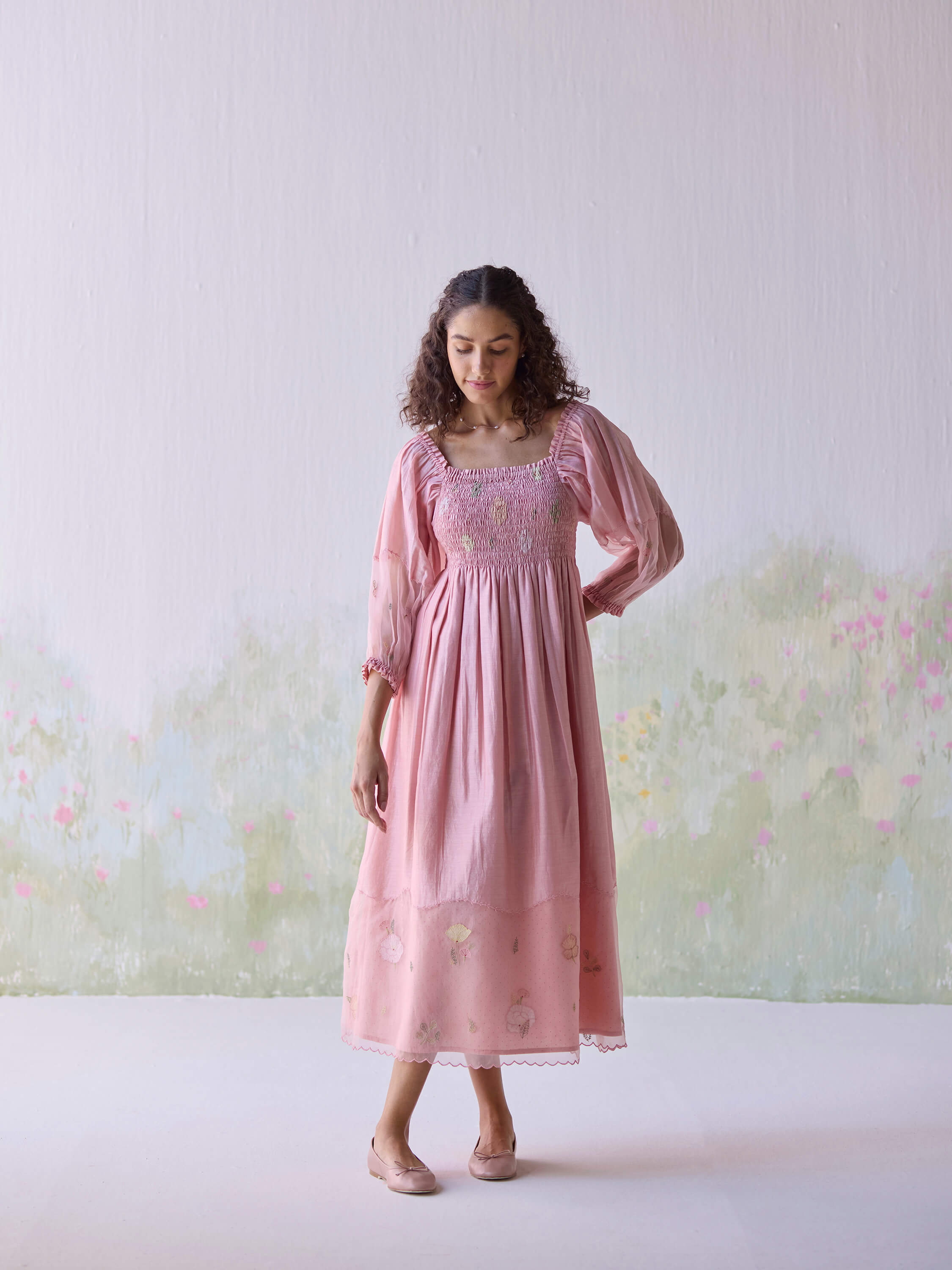 Woman in pink floral maxi dress standing against a pastel floral background.