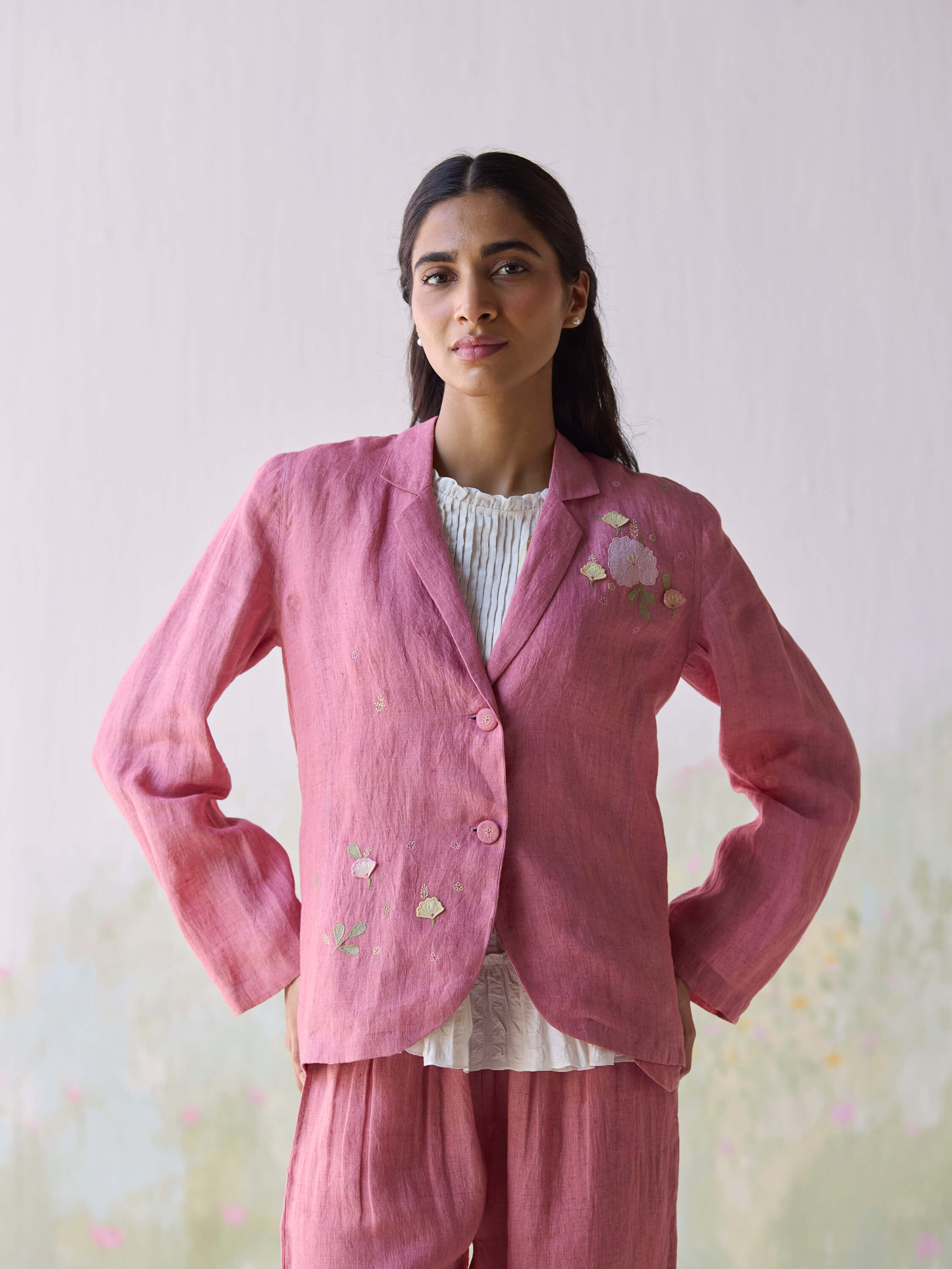 Woman in pink embroidered suit jacket and trousers against a light backdrop.