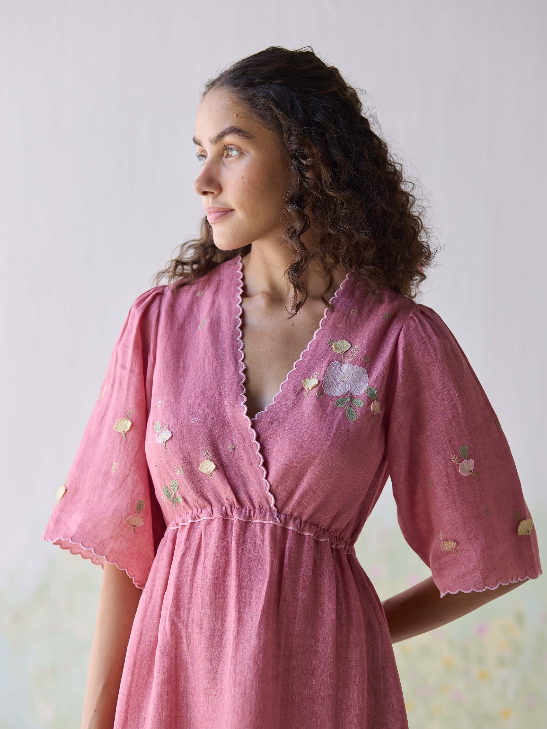 Woman wearing pink embroidered dress looking into the distance.