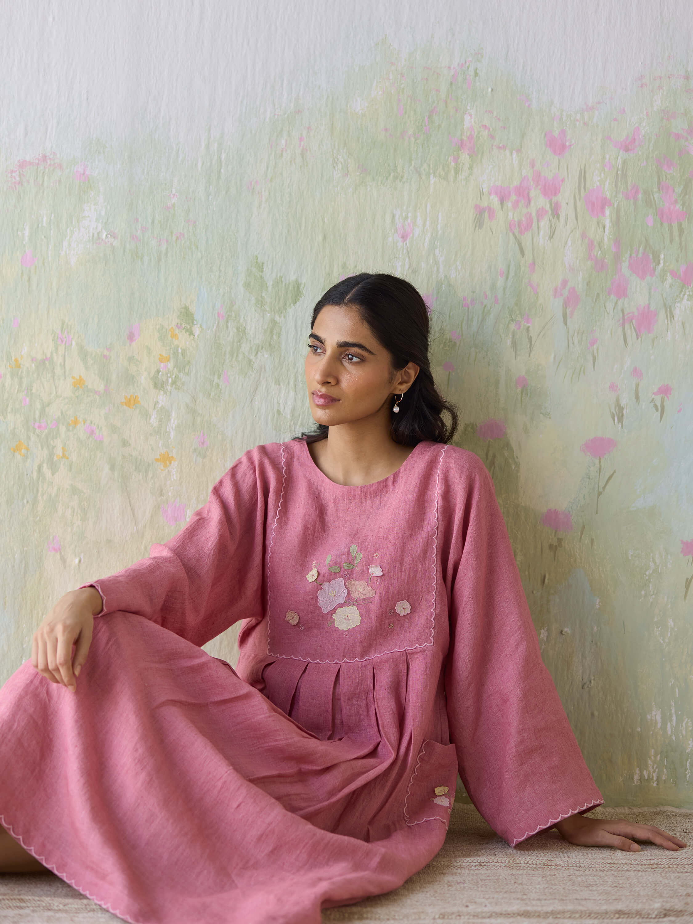 Woman in pink dress sitting against a floral painted wall.