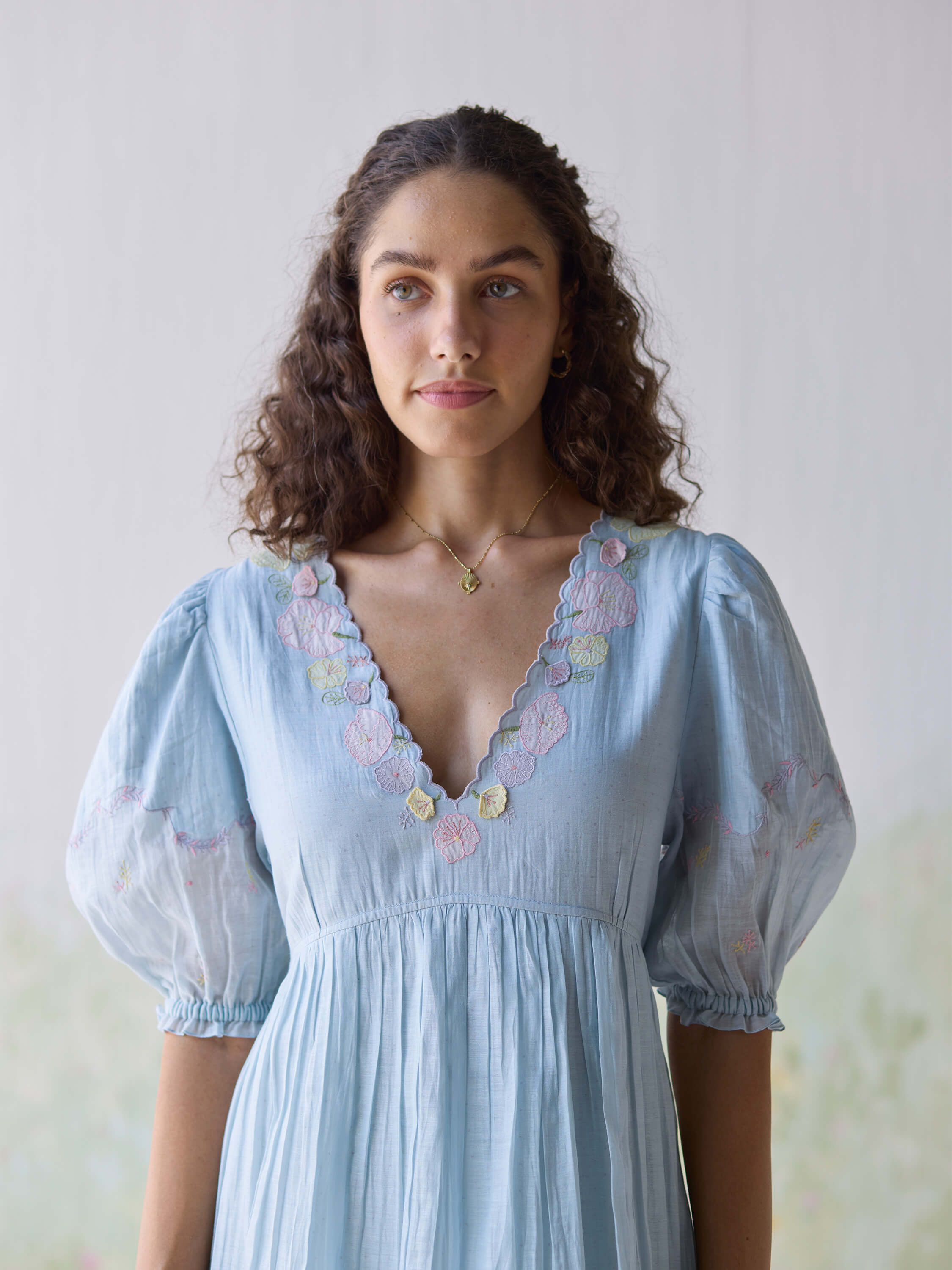 Woman wearing light blue dress with floral embroidery details.