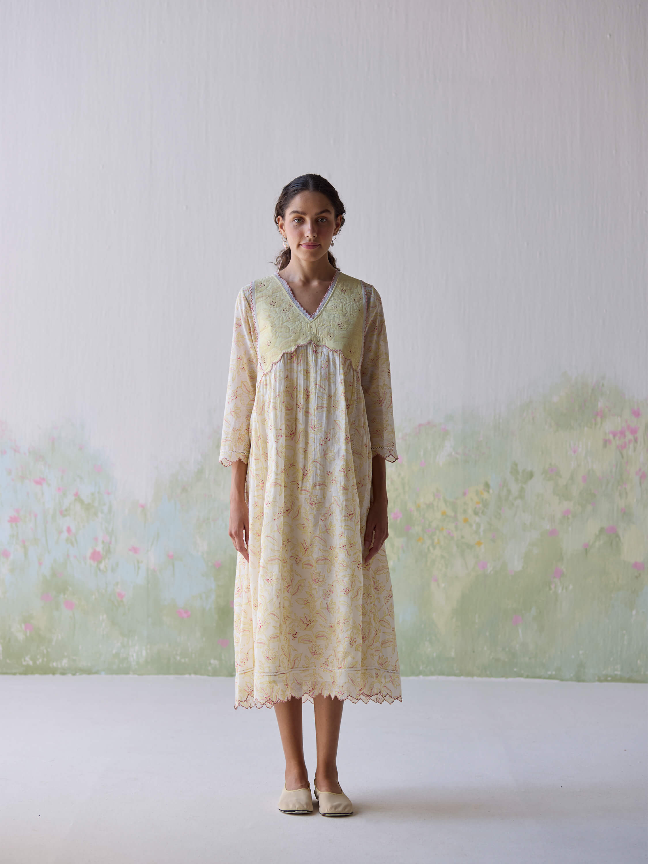 Woman in floral pastel dress standing against a minimalistic background.