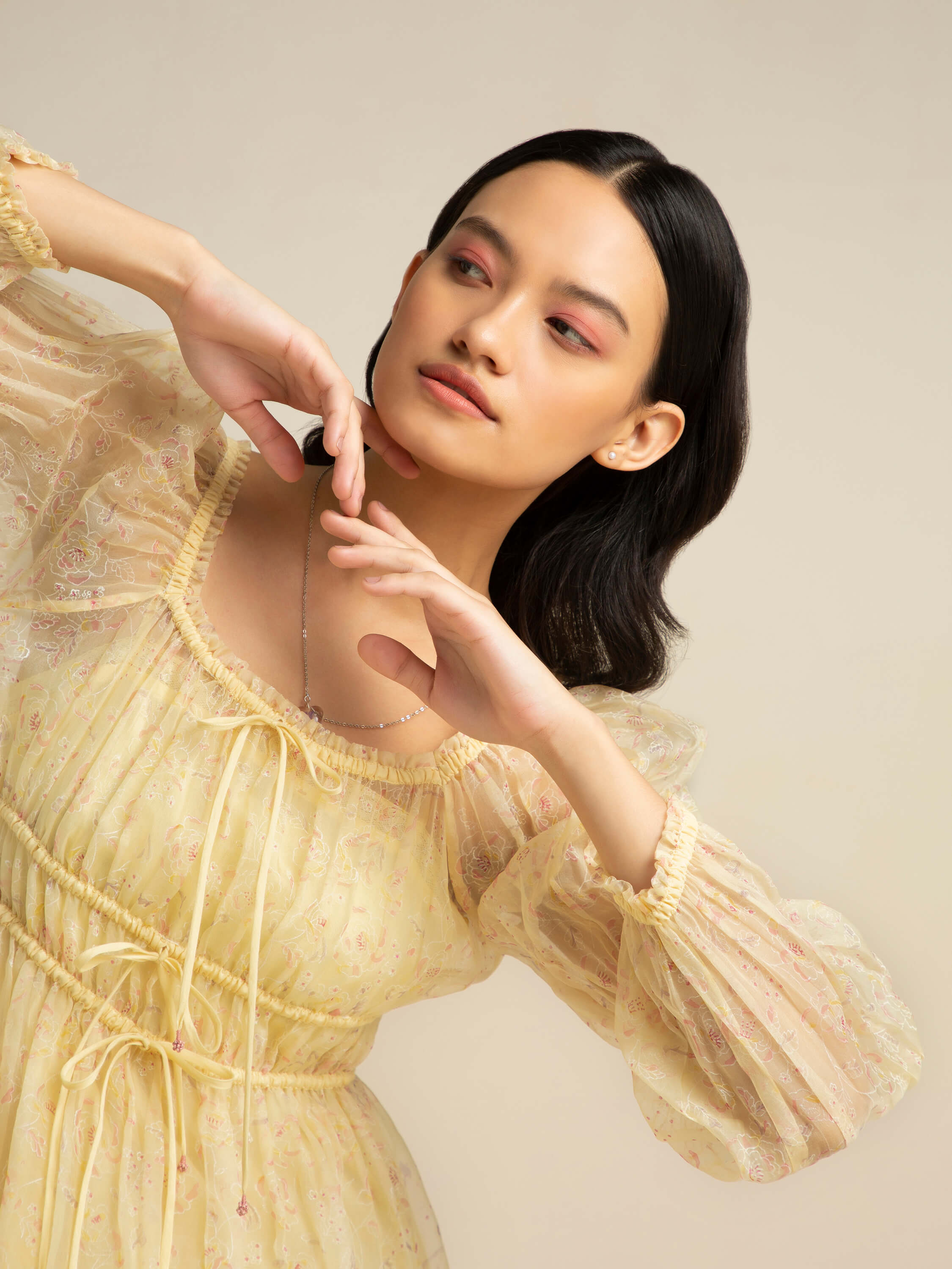 Woman wearing pastel yellow dress with sheer sleeves posing elegantly.