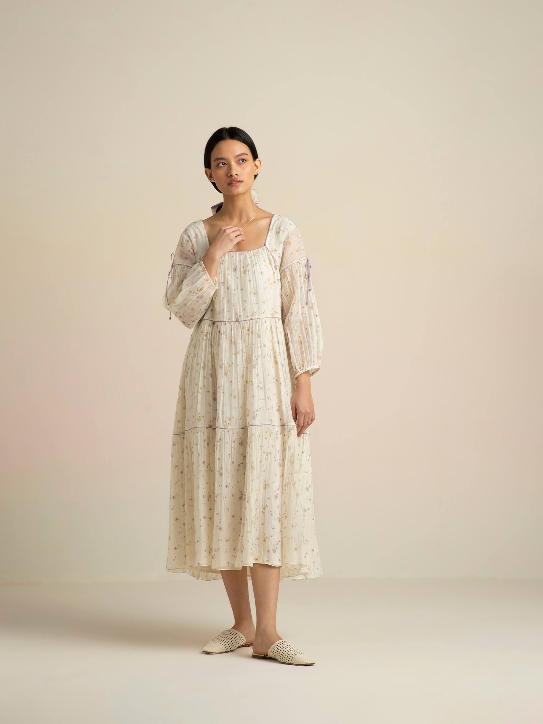 Woman in floral white dress and white flats posing against neutral background.