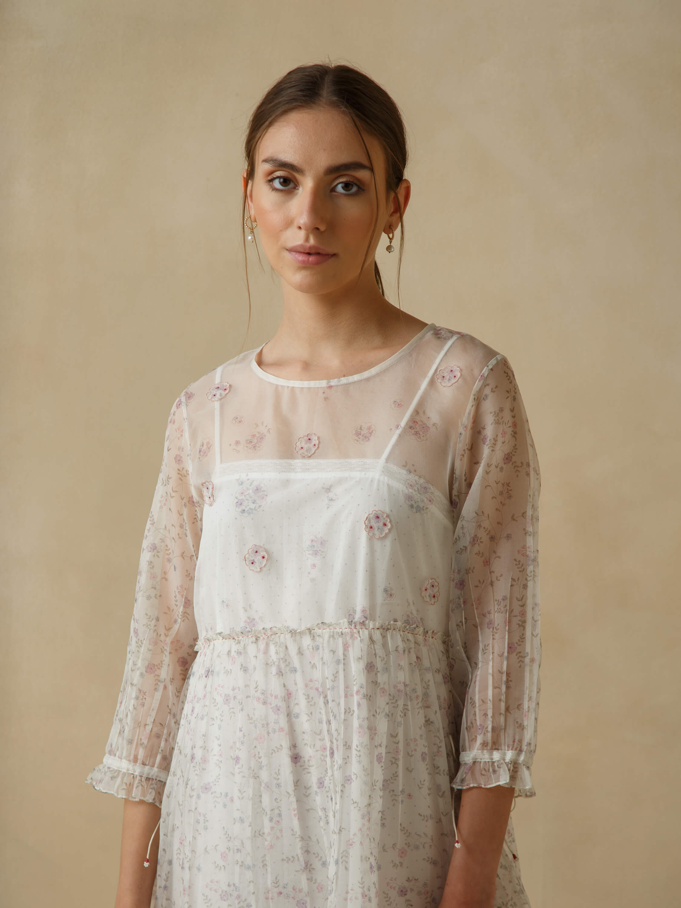 A woman wearing a sheer floral dress against a beige background.