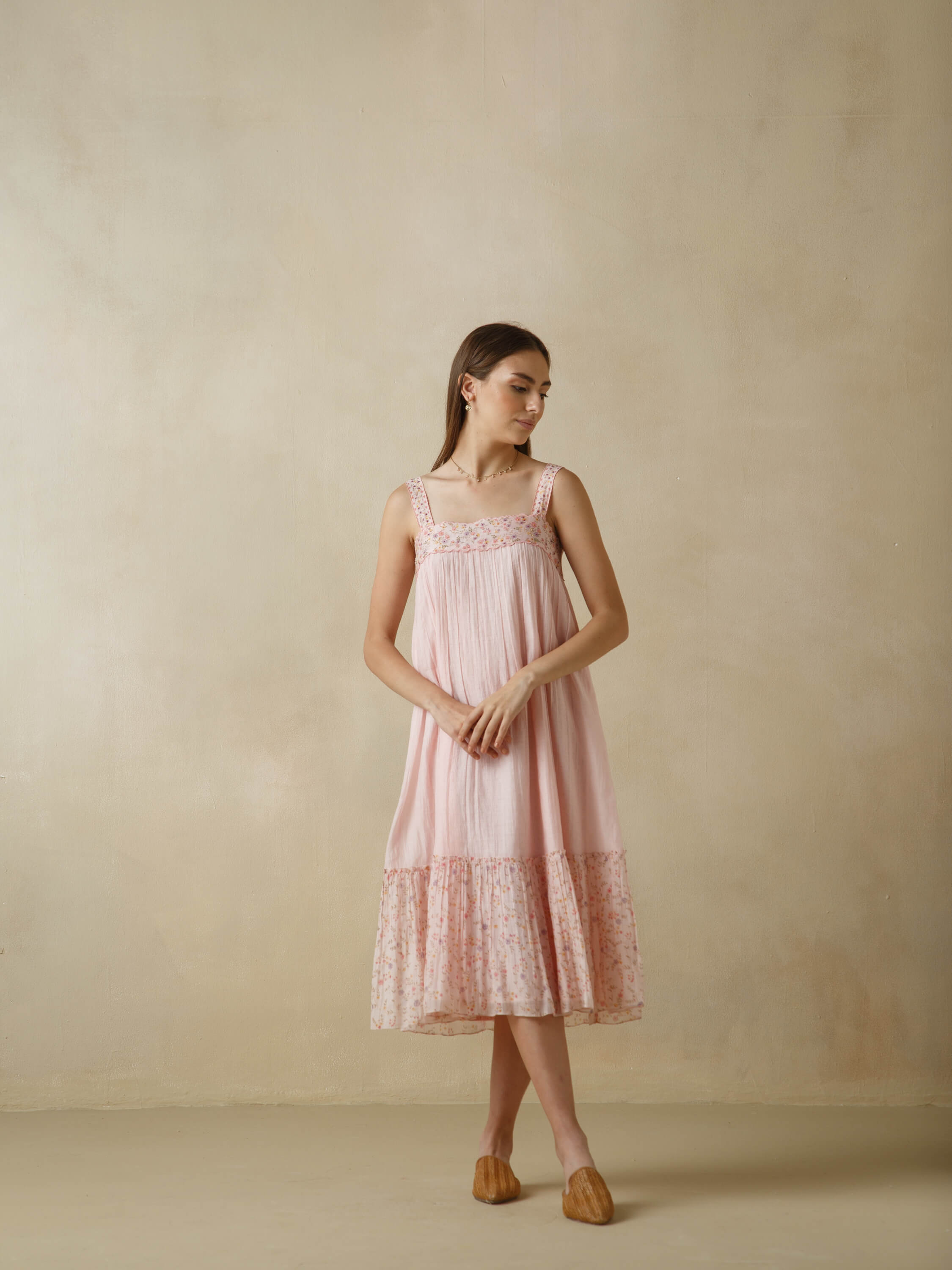 Woman in pink sleeveless dress standing against neutral wall background.