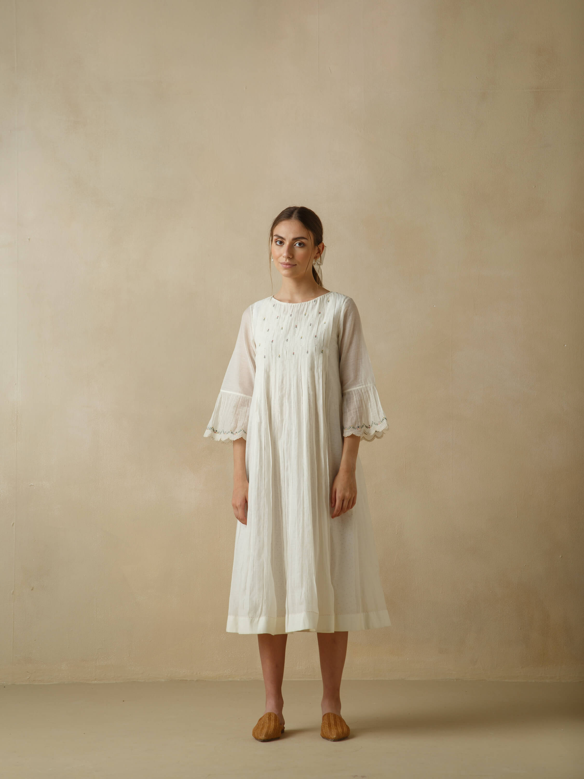 Woman in a white dress posing against a beige background.