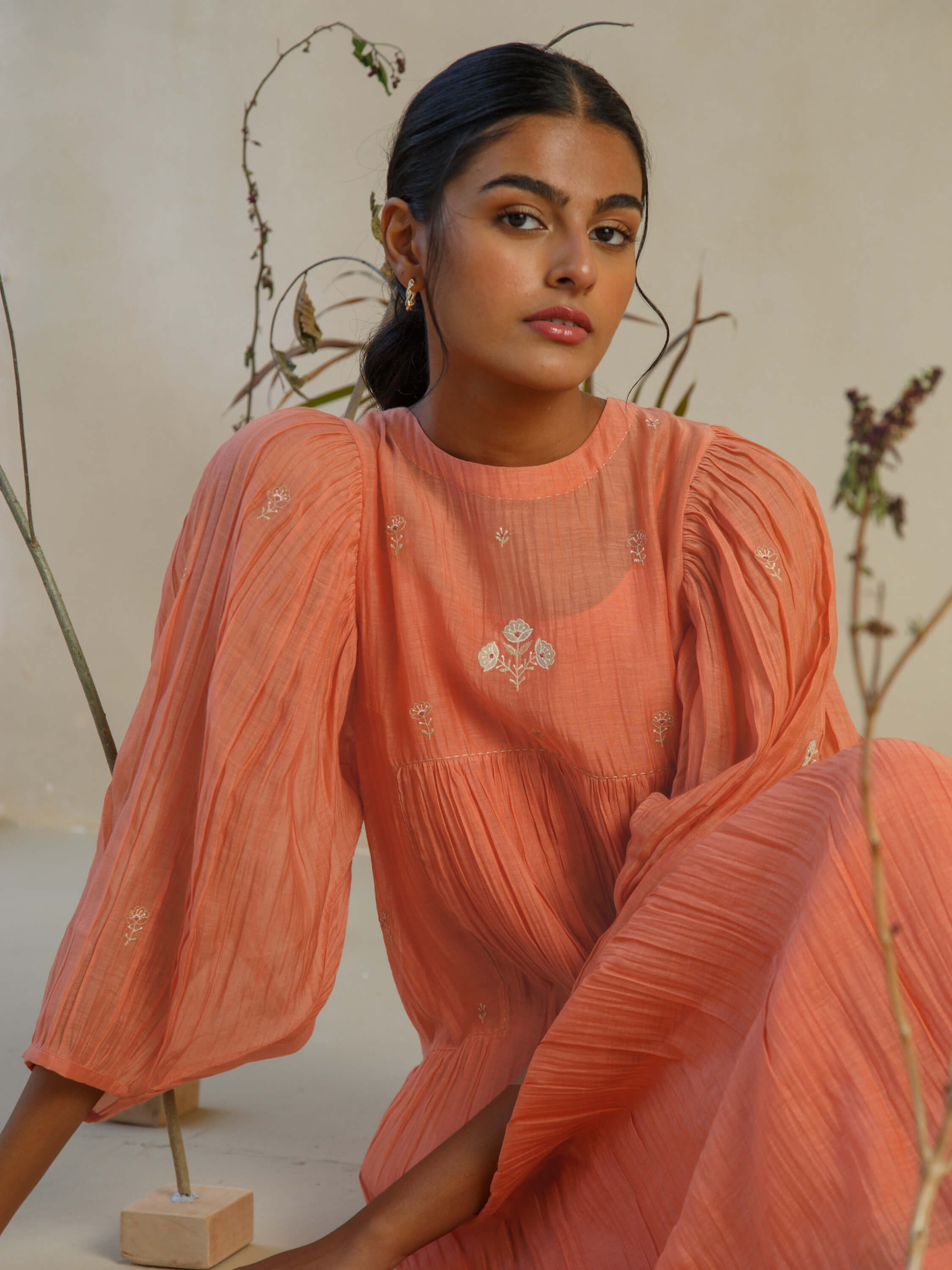 Woman in an orange long-sleeve dress with embroidered floral details.