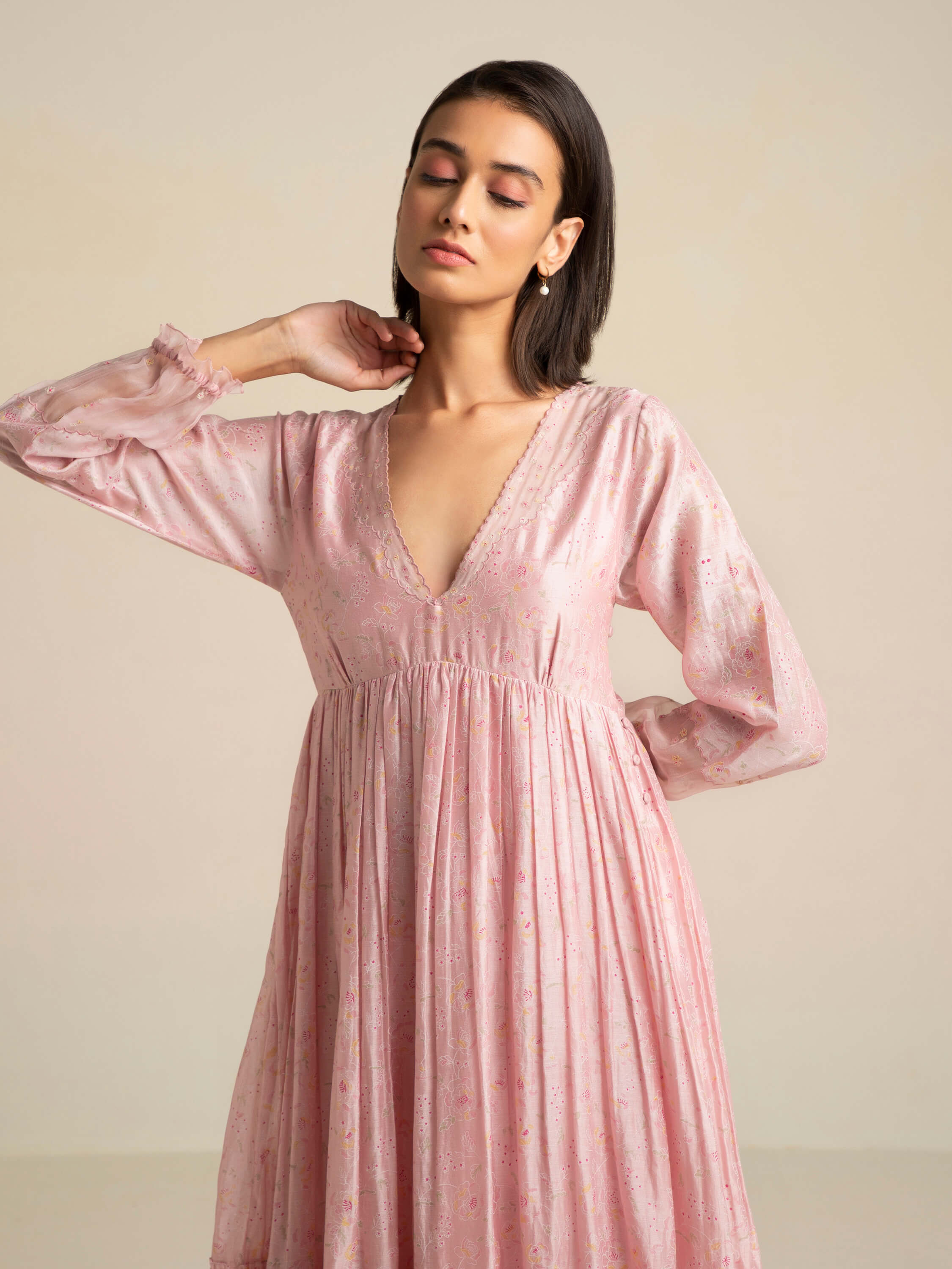 Woman in pink V-neck dress posing elegantly with closed eyes.