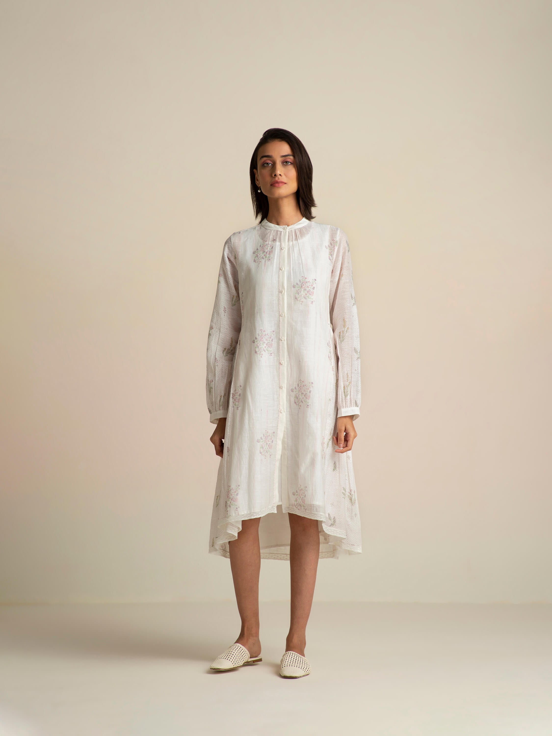 Woman in white long-sleeve floral dress and white slip-on shoes.