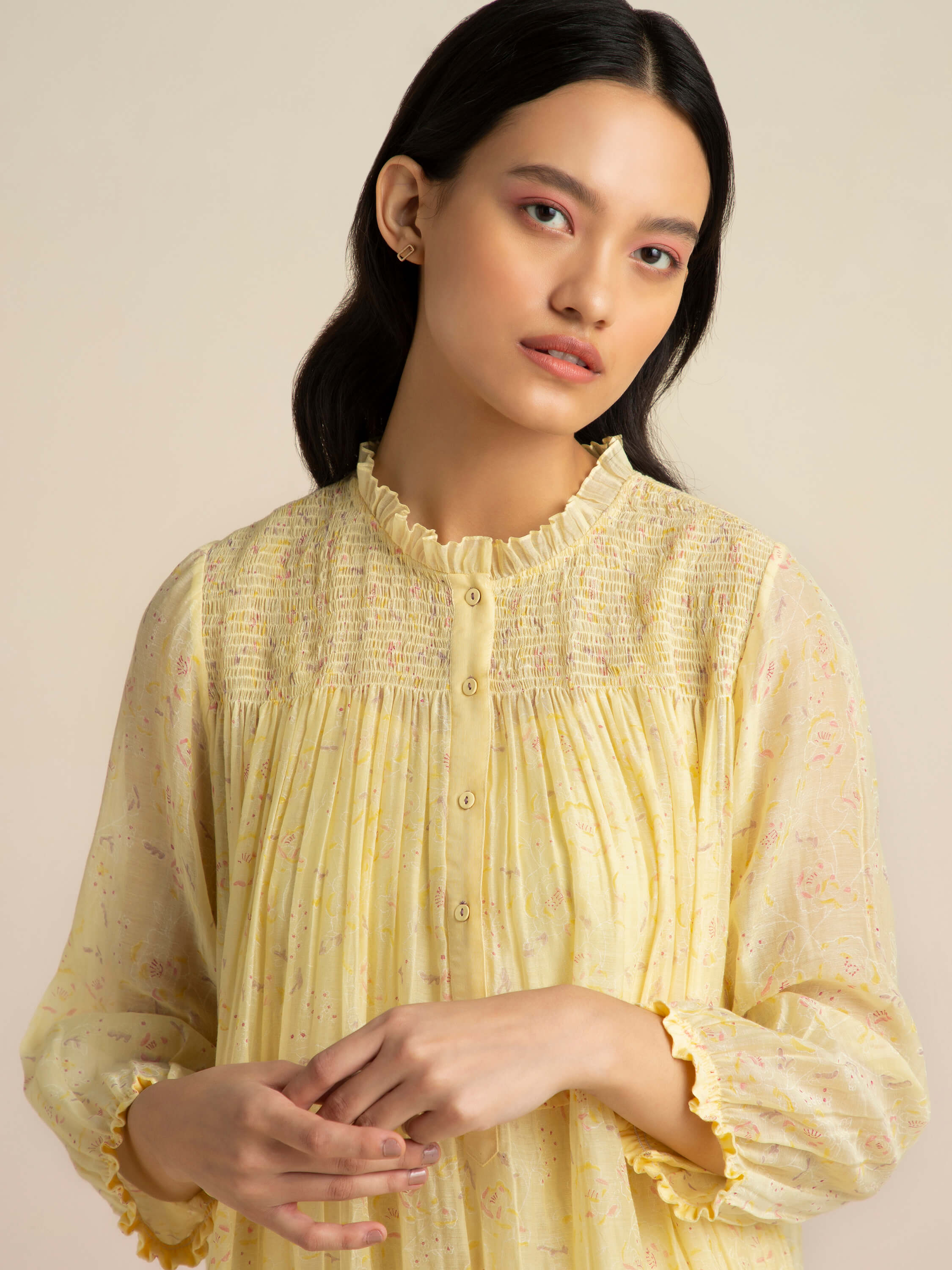 Woman in a yellow floral dress with a neutral background.