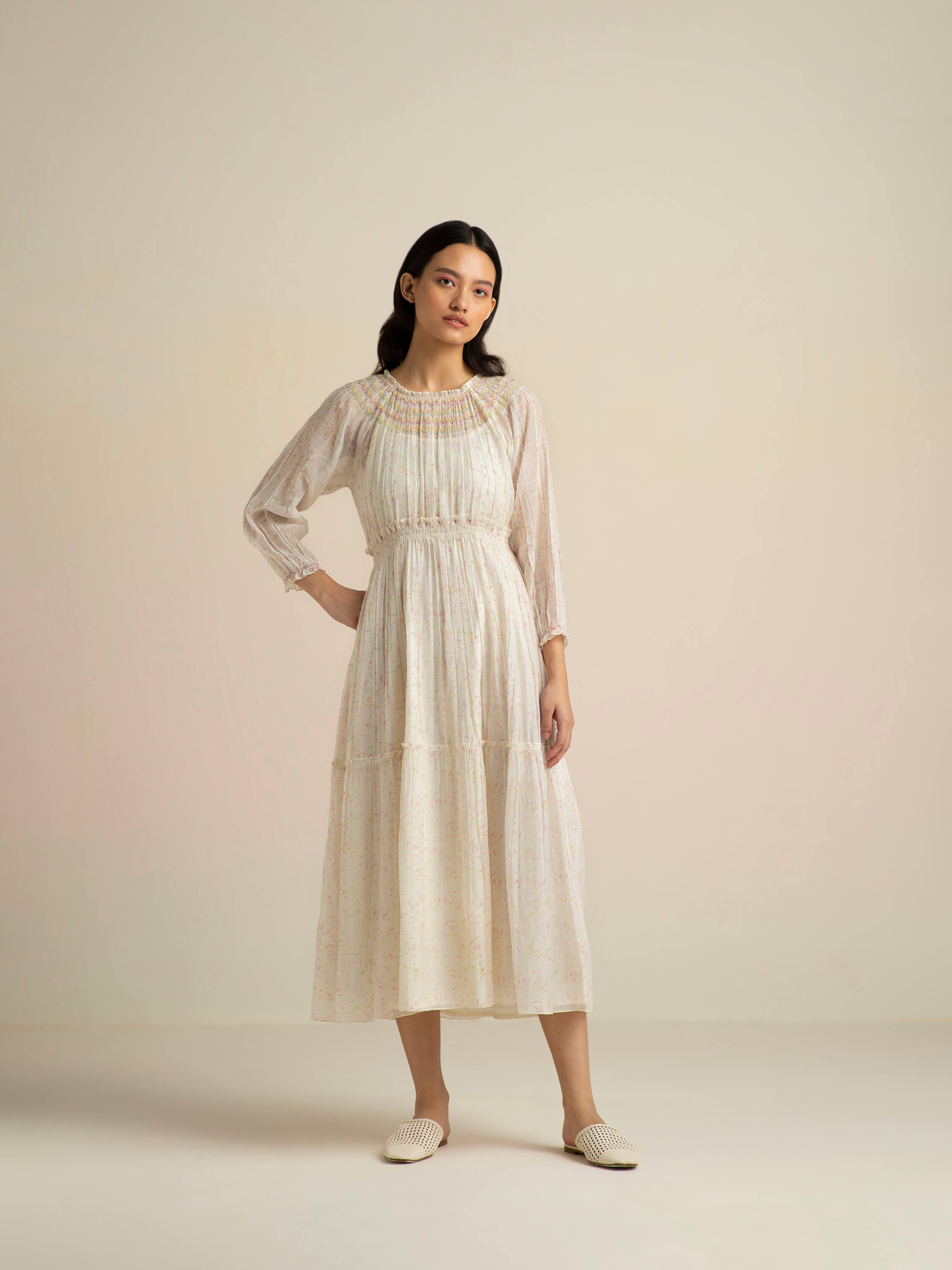 Woman wearing a beige, long-sleeve, floral midi dress with white mules.