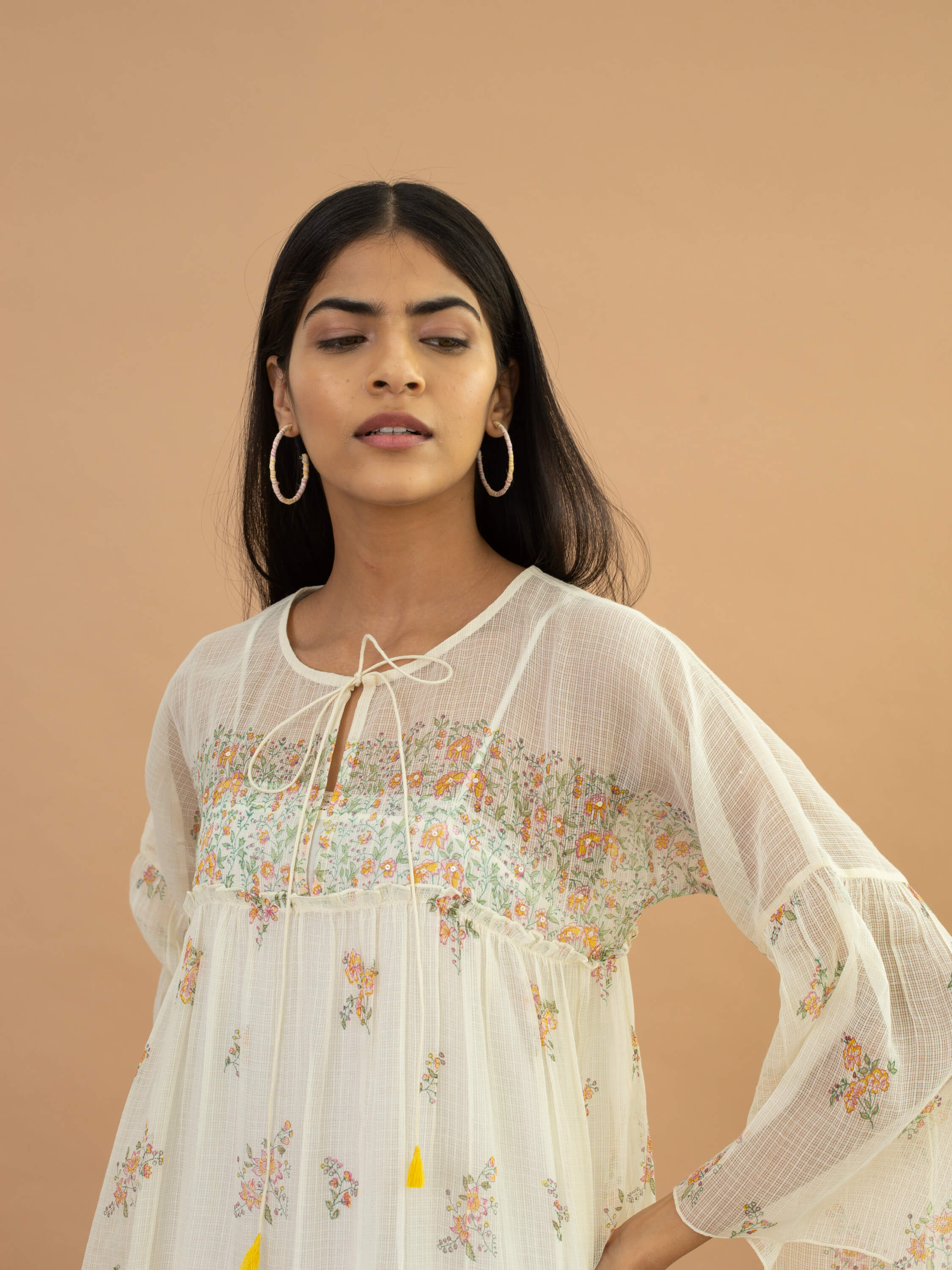 Woman in floral dress and hoop earrings against beige background.