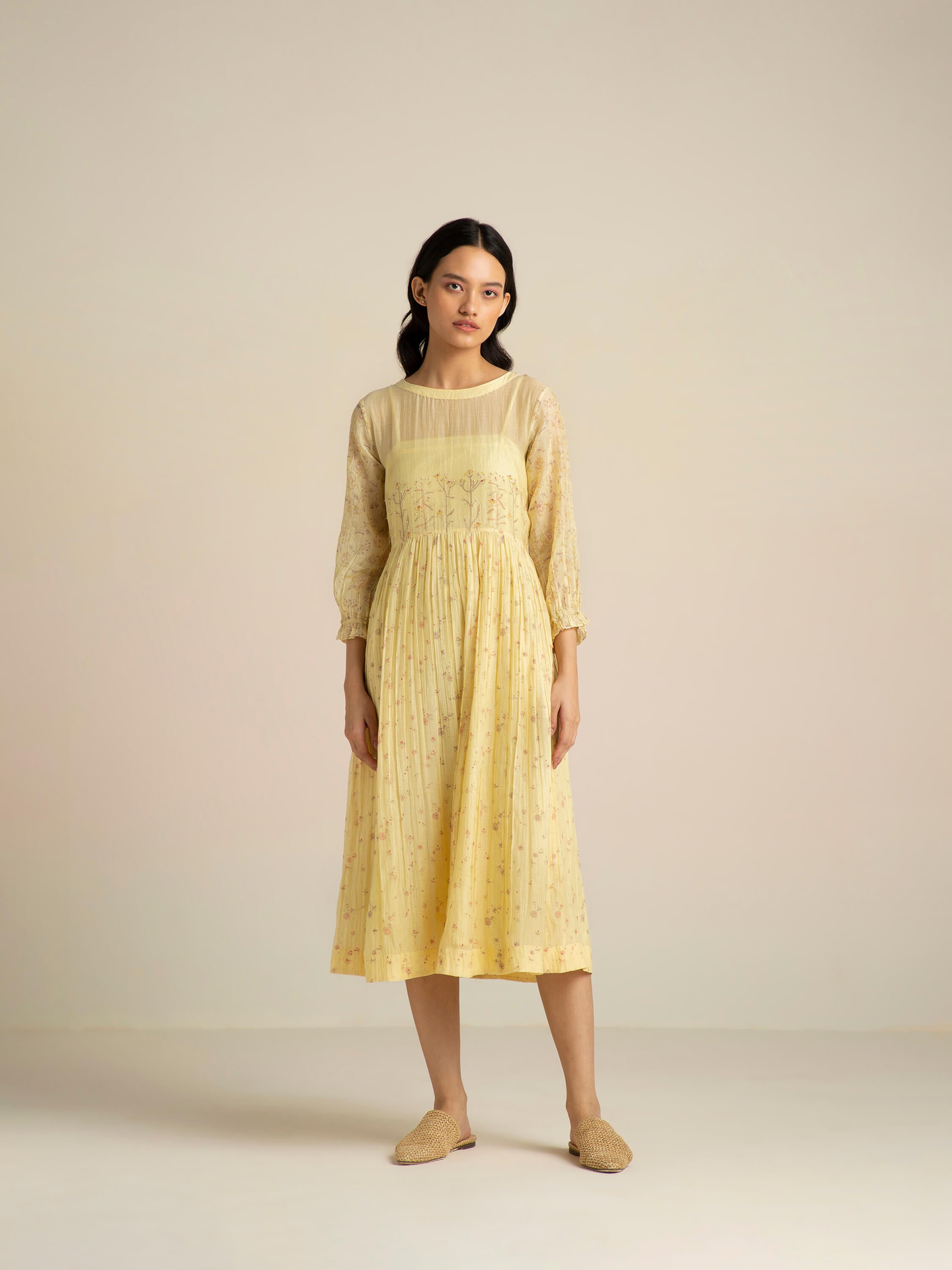 Woman in yellow floral dress standing against plain background.