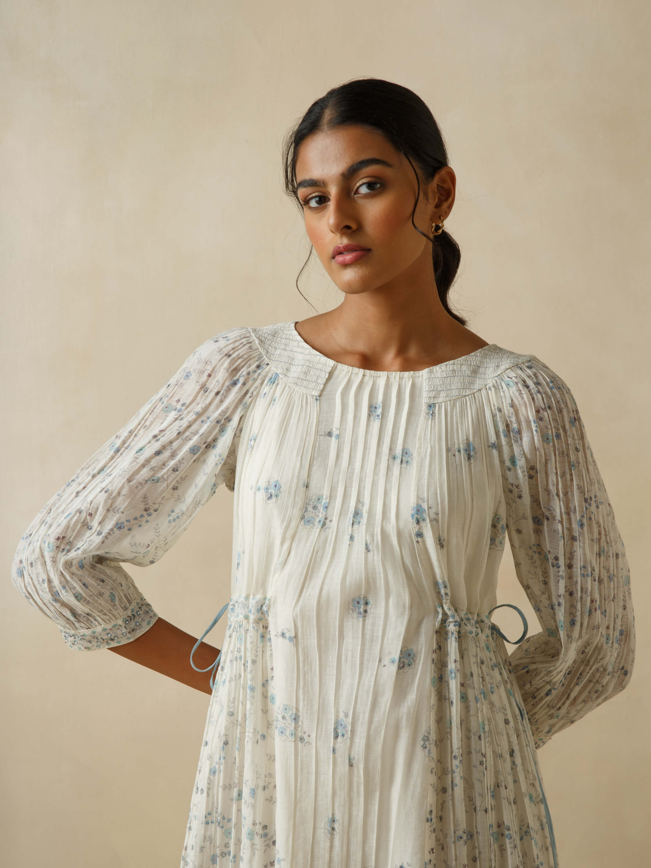 Woman wearing white floral dress with pleats and sheer sleeves.