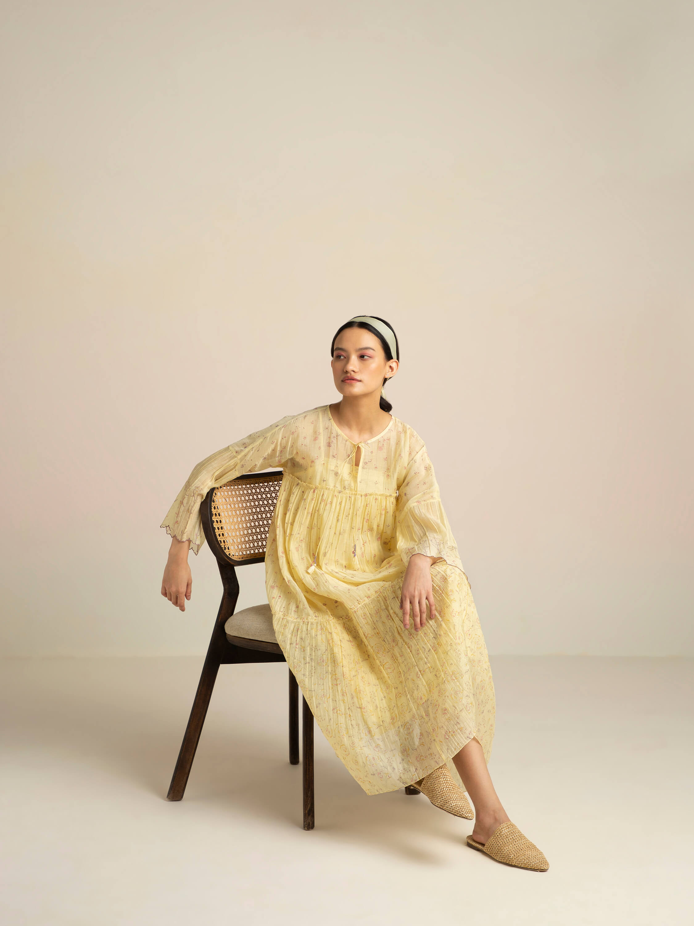 Woman in yellow dress sitting on a wooden chair.