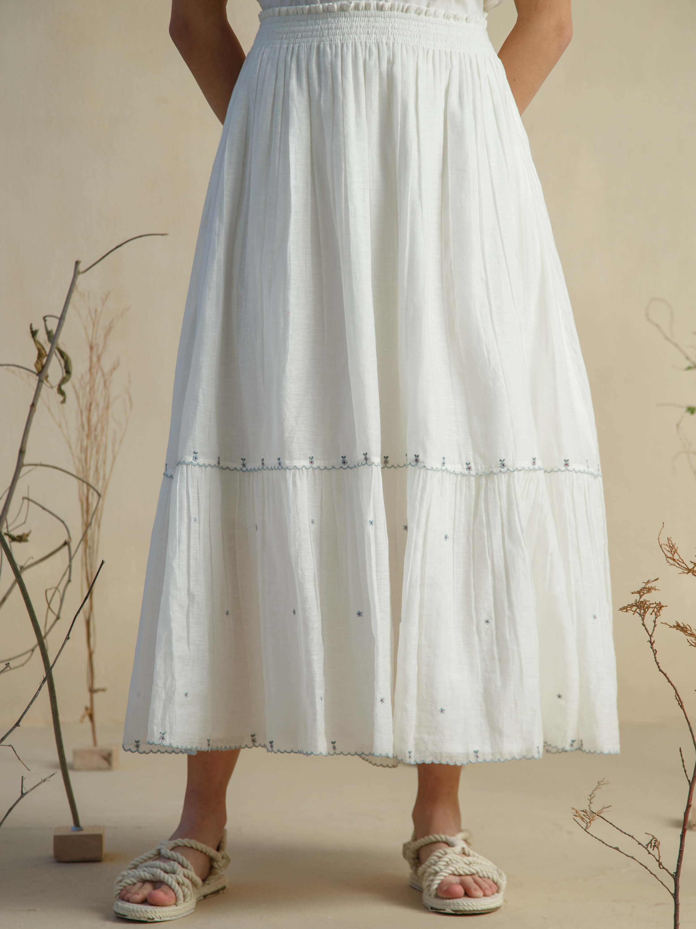 Woman wearing a white embroidered midi skirt and woven sandals.