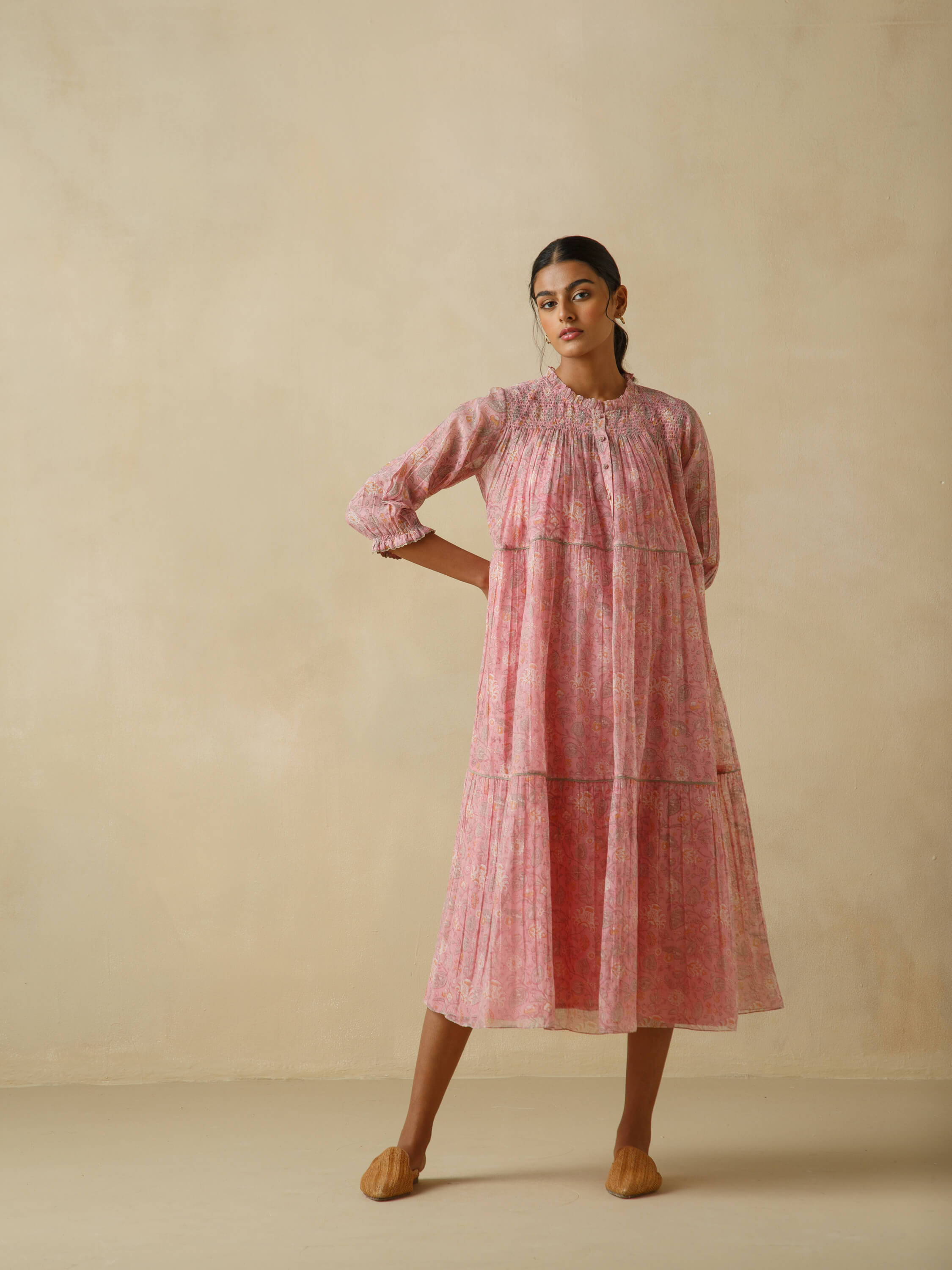 Woman wearing a flowing pink floral dress in a neutral background.