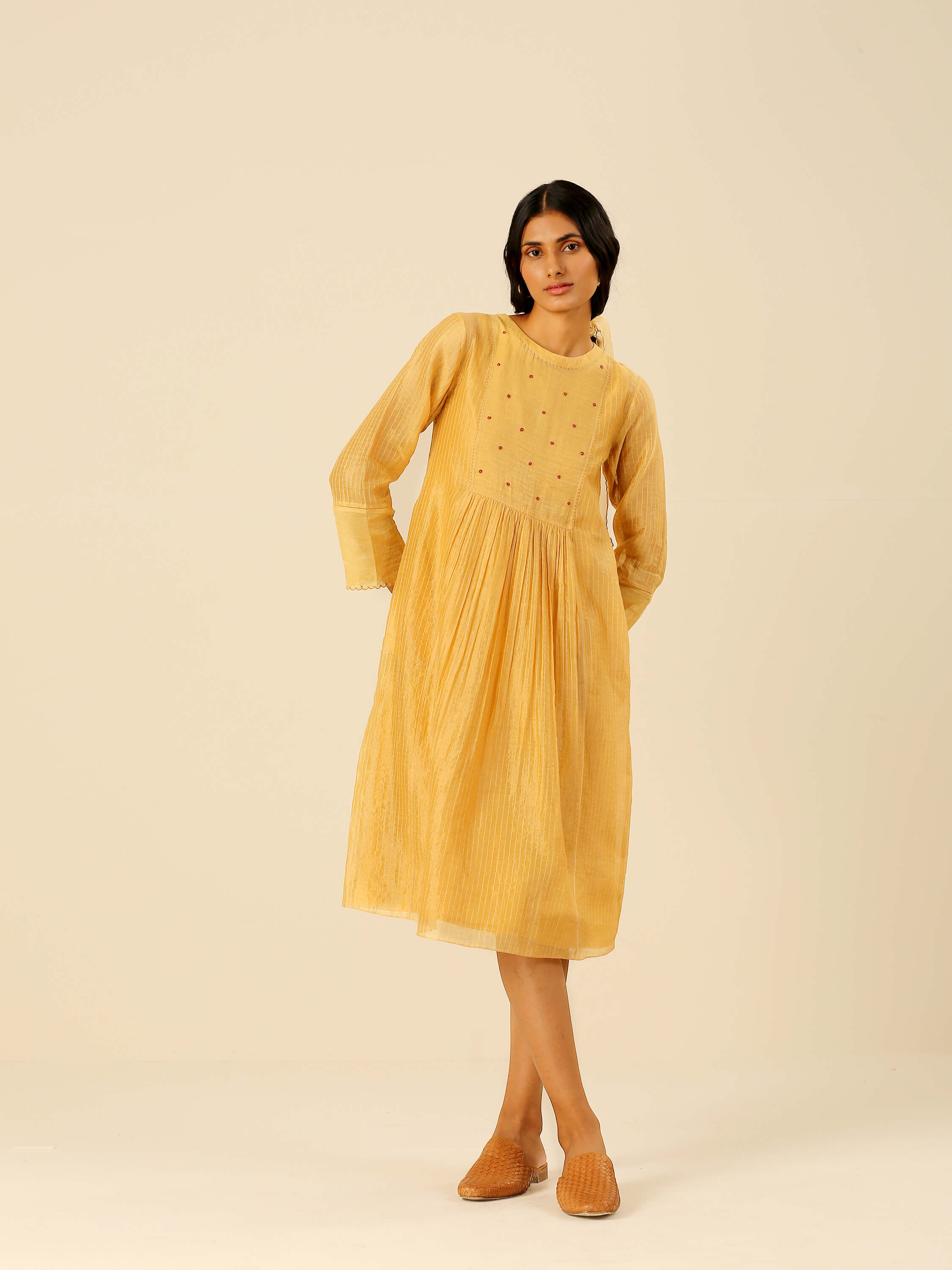 Woman in a yellow midi dress with woven mules posing.