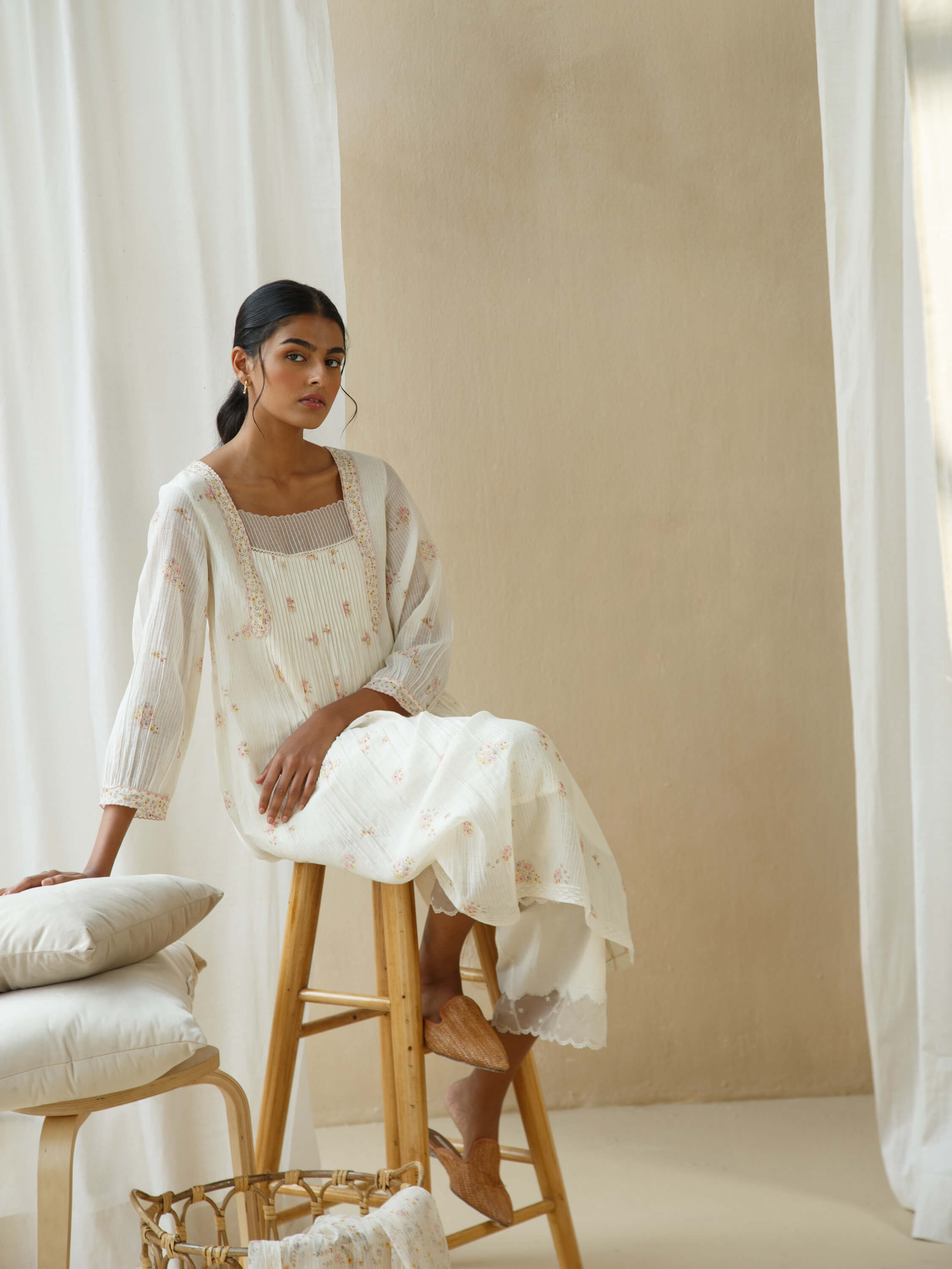 Woman in white dress sitting on wooden stool in minimalist room.