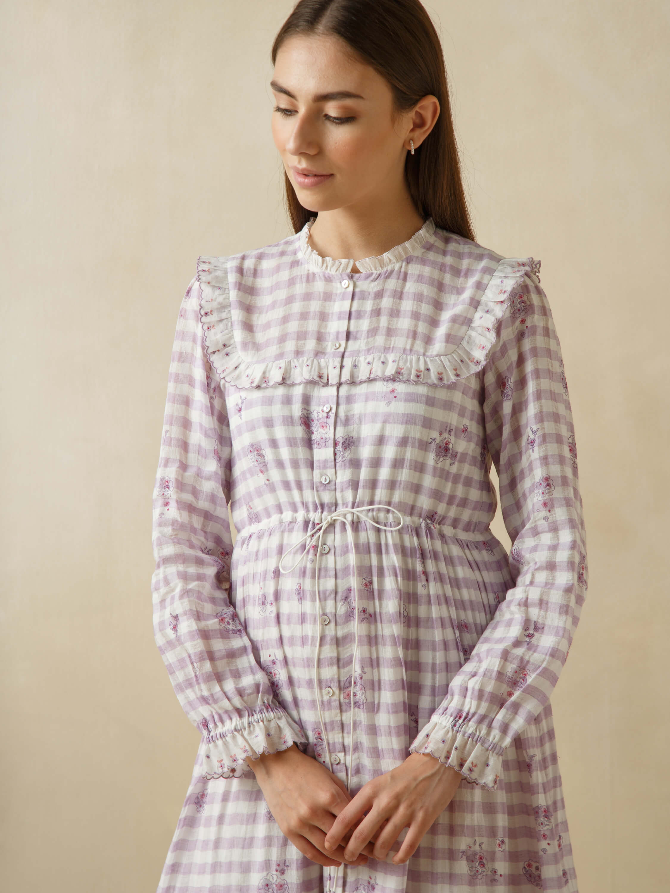 Woman in a lilac checkered dress with floral design and white frills.