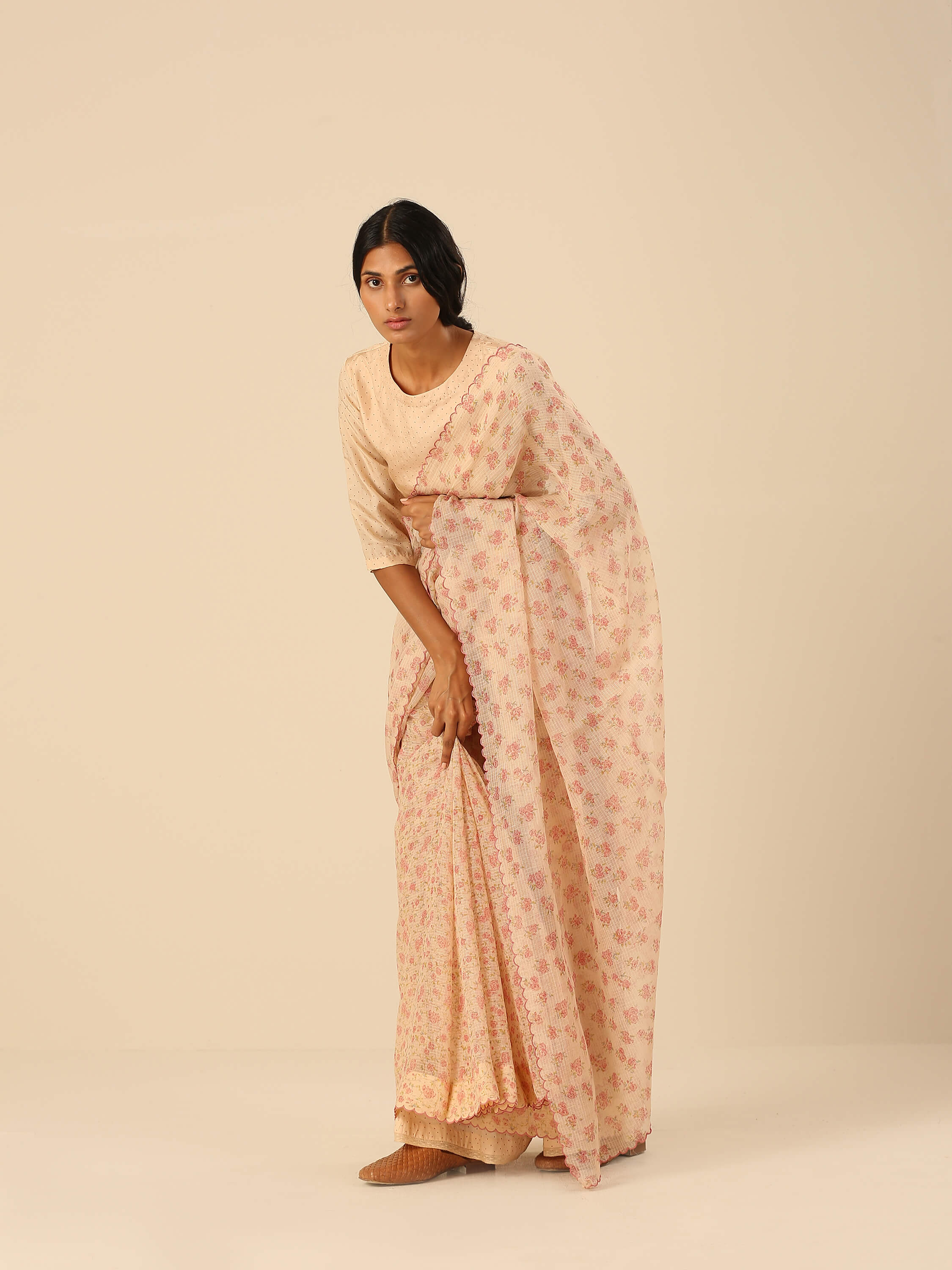 Woman in elegant beige and floral saree, looking down.