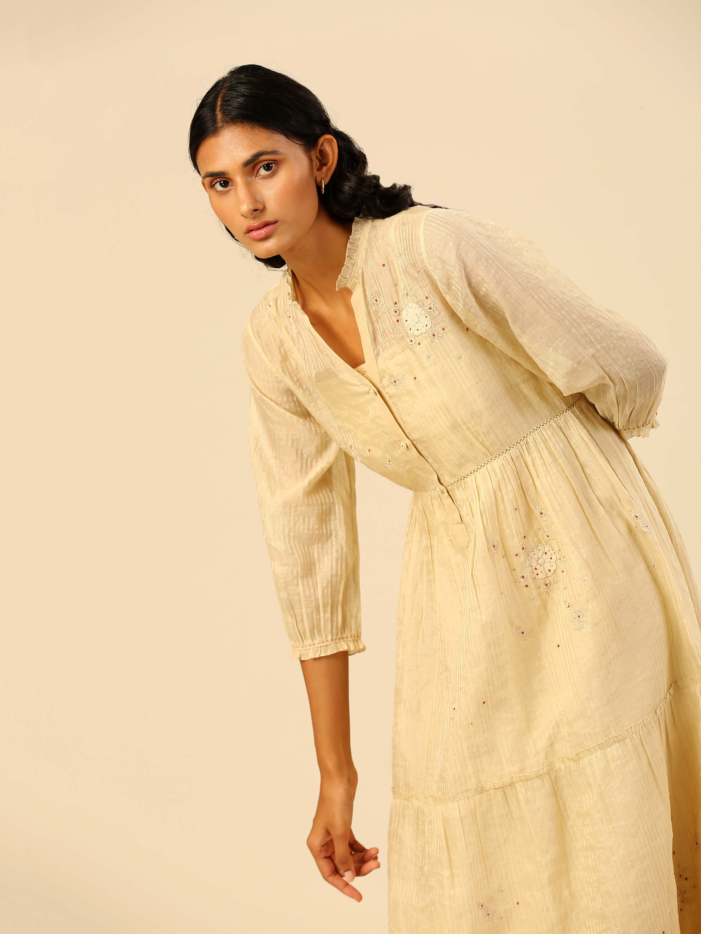 Woman in a beige embroidered dress with long sleeves.