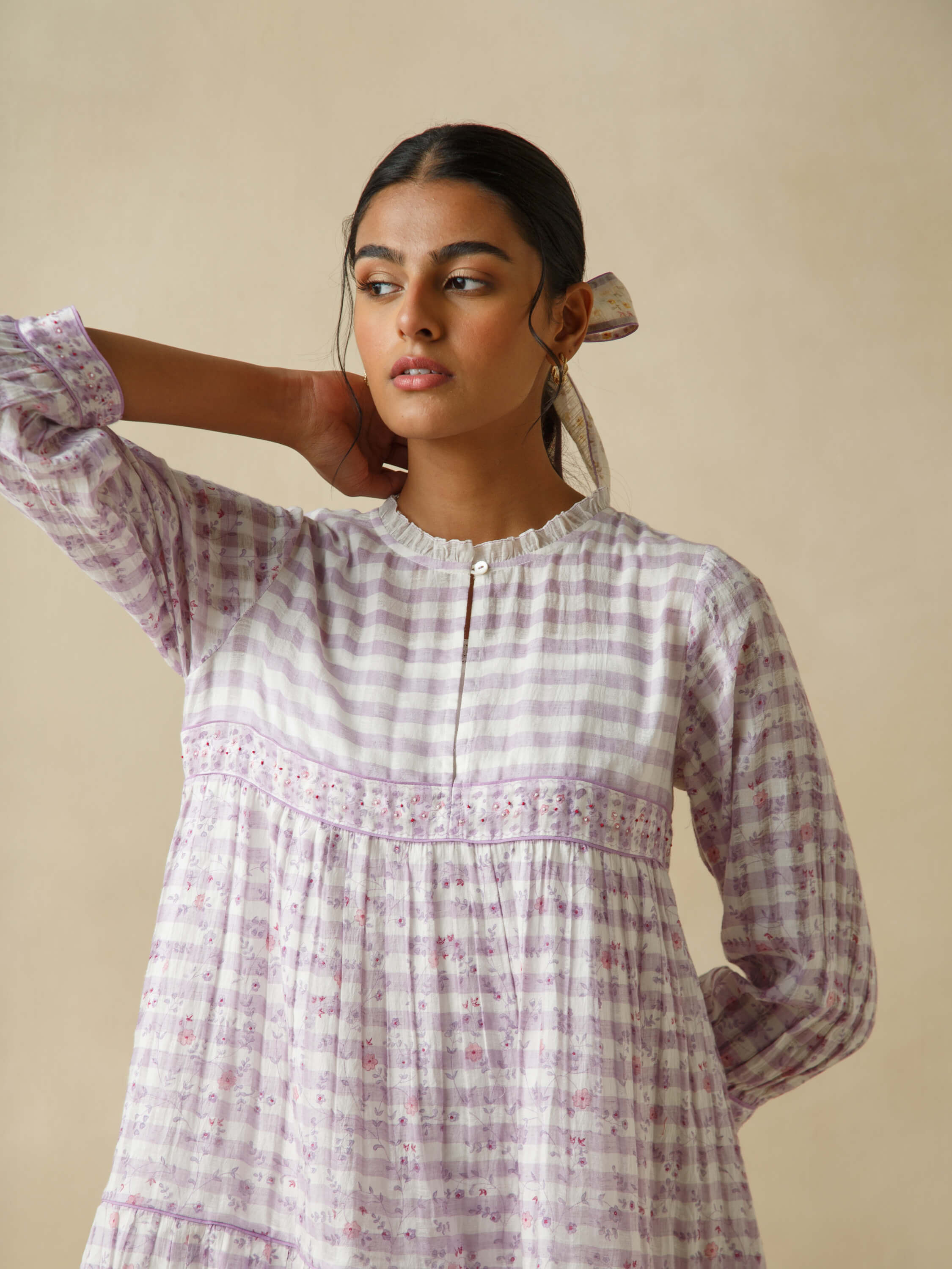 Woman in a checked and floral dress with a pensive look.