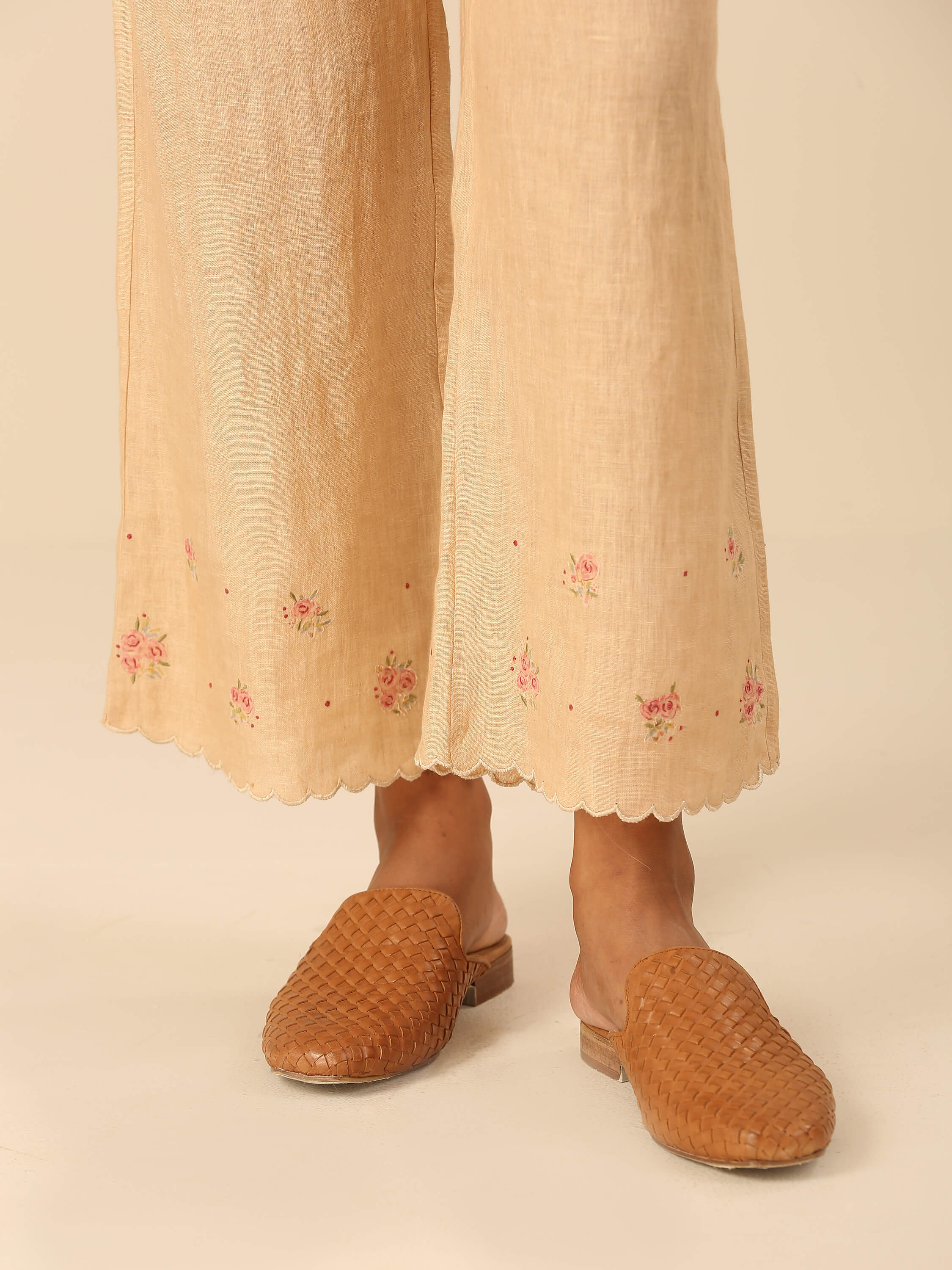 Close-up of embroidered palazzo pants with woven brown slip-on shoes.