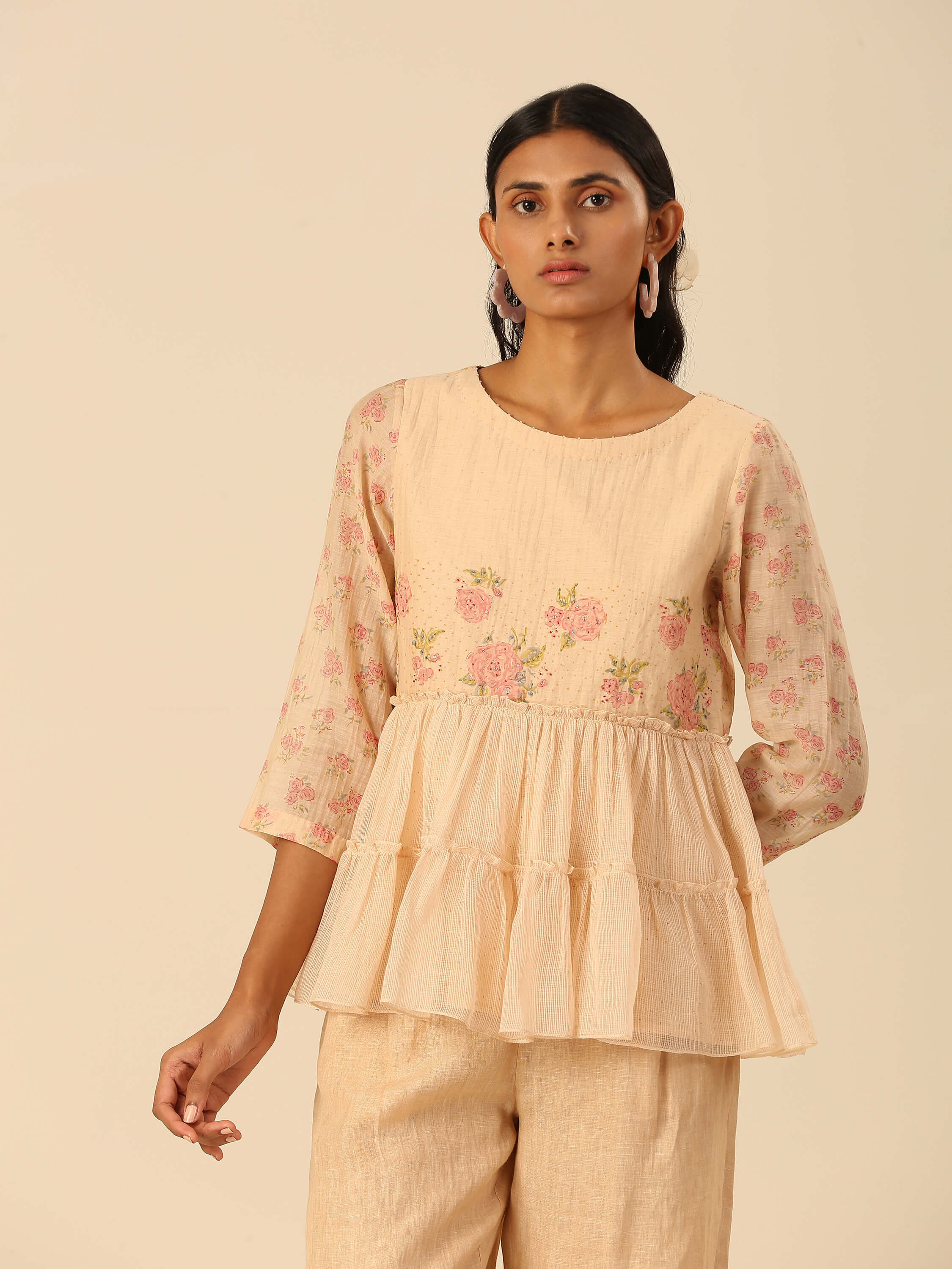 Woman wearing a beige floral top with ruffle hem.