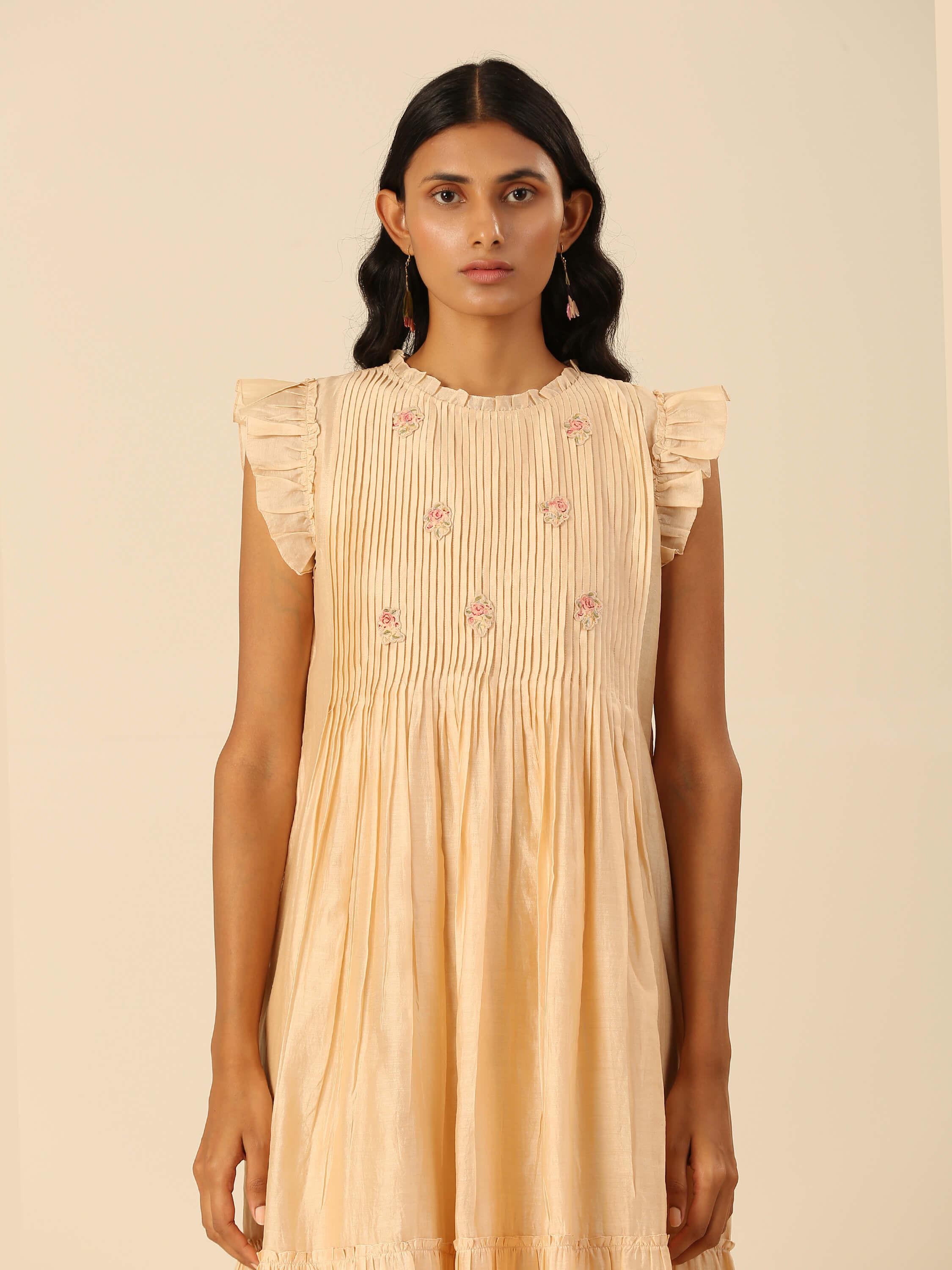 Young woman modeling beige embroidered dress with ruffled sleeves.