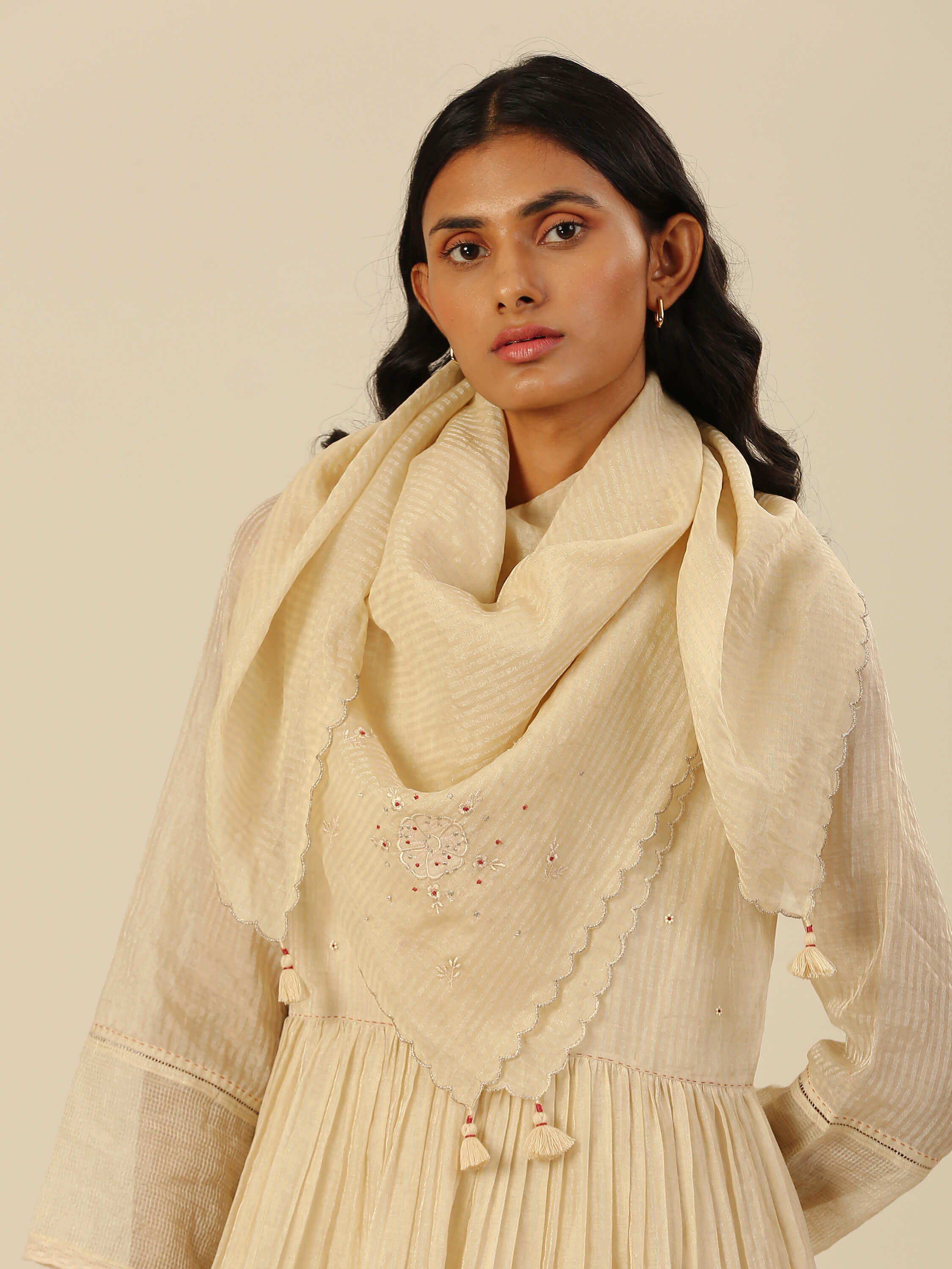 Woman wearing beige traditional attire with embroidered shawl.