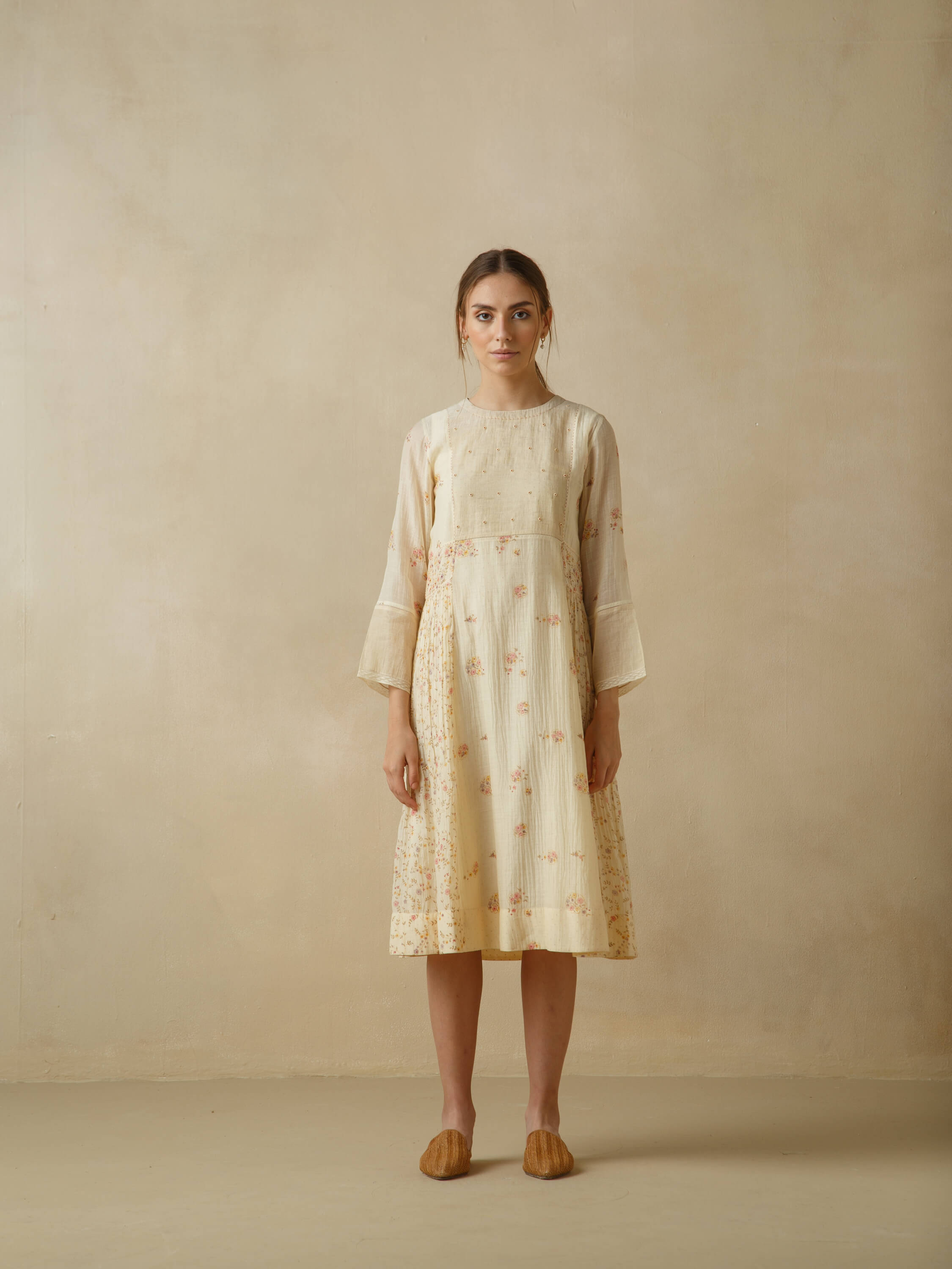 Woman wearing a cream floral dress standing against a beige backdrop.