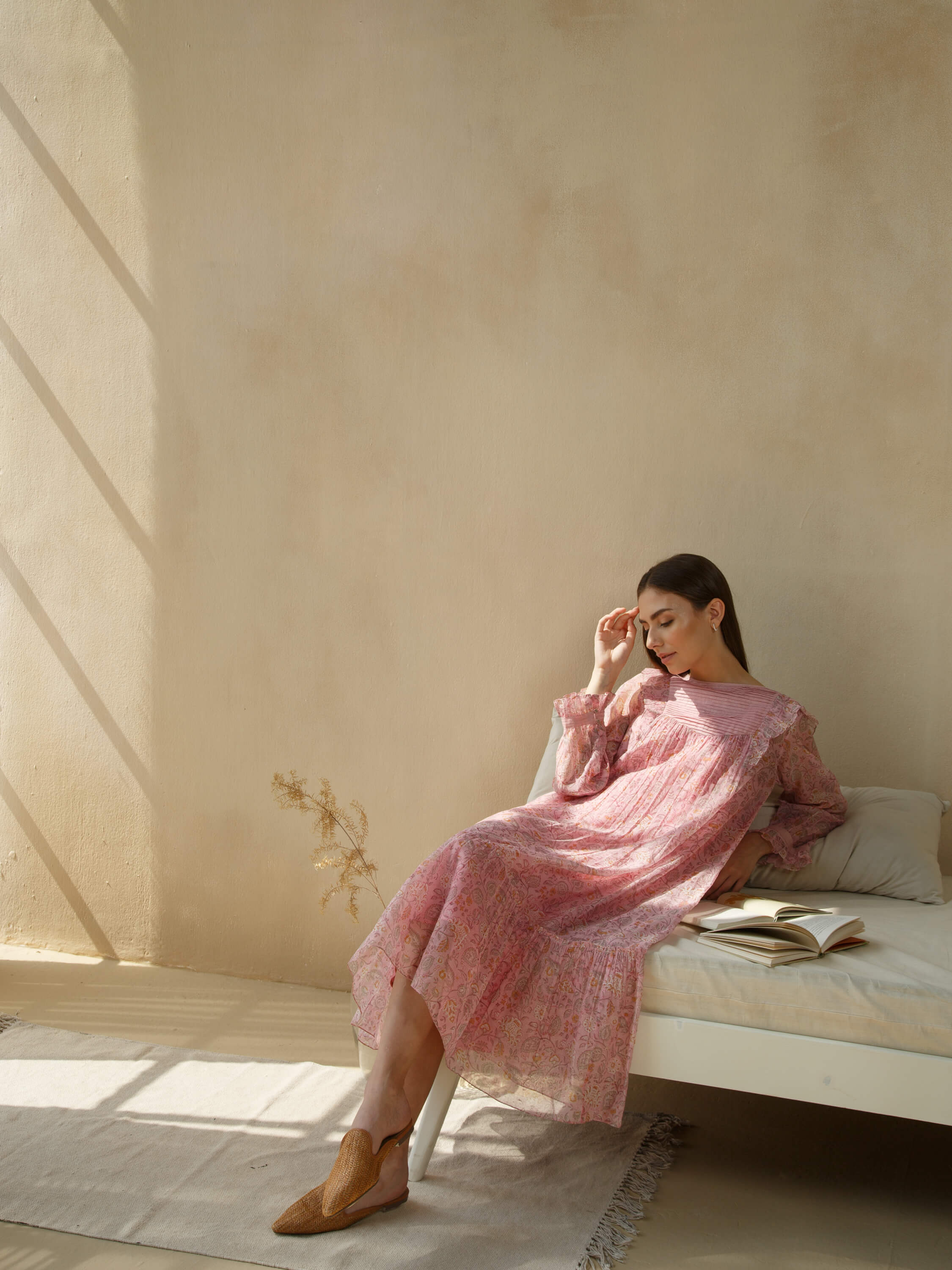 Woman relaxing on a bed in sunlight, wearing a pink floral dress.